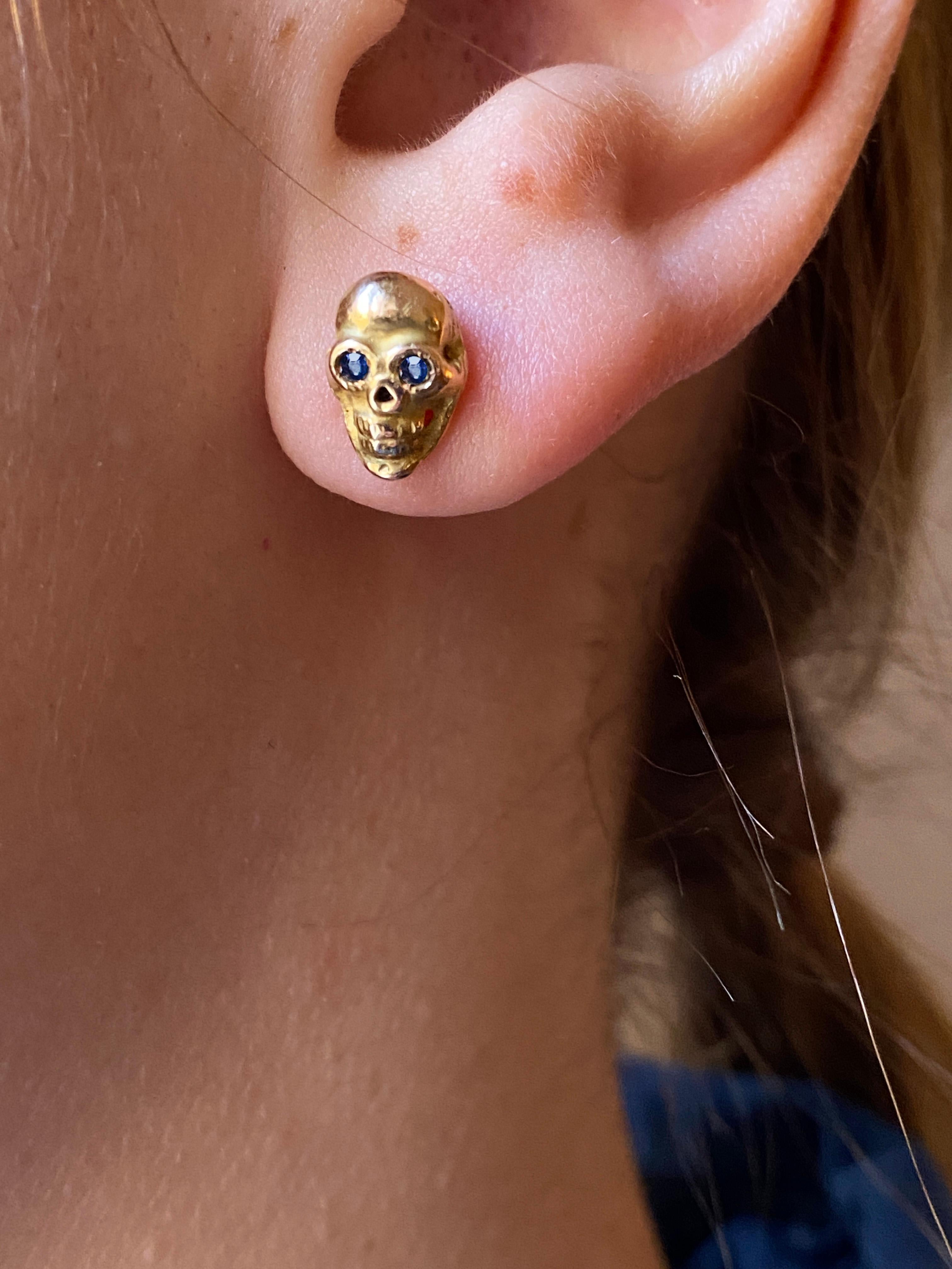 Victorian Style 18K Yellow Gold Blue Sapphire Eyes Rock Stud Skull Man Earrings. 18K yellow gold men’s stud earrings in the shape of a skull. The 18K Gold earrings feature blue sapphire eyes and depict the skull of a skeleton. With their bold design
