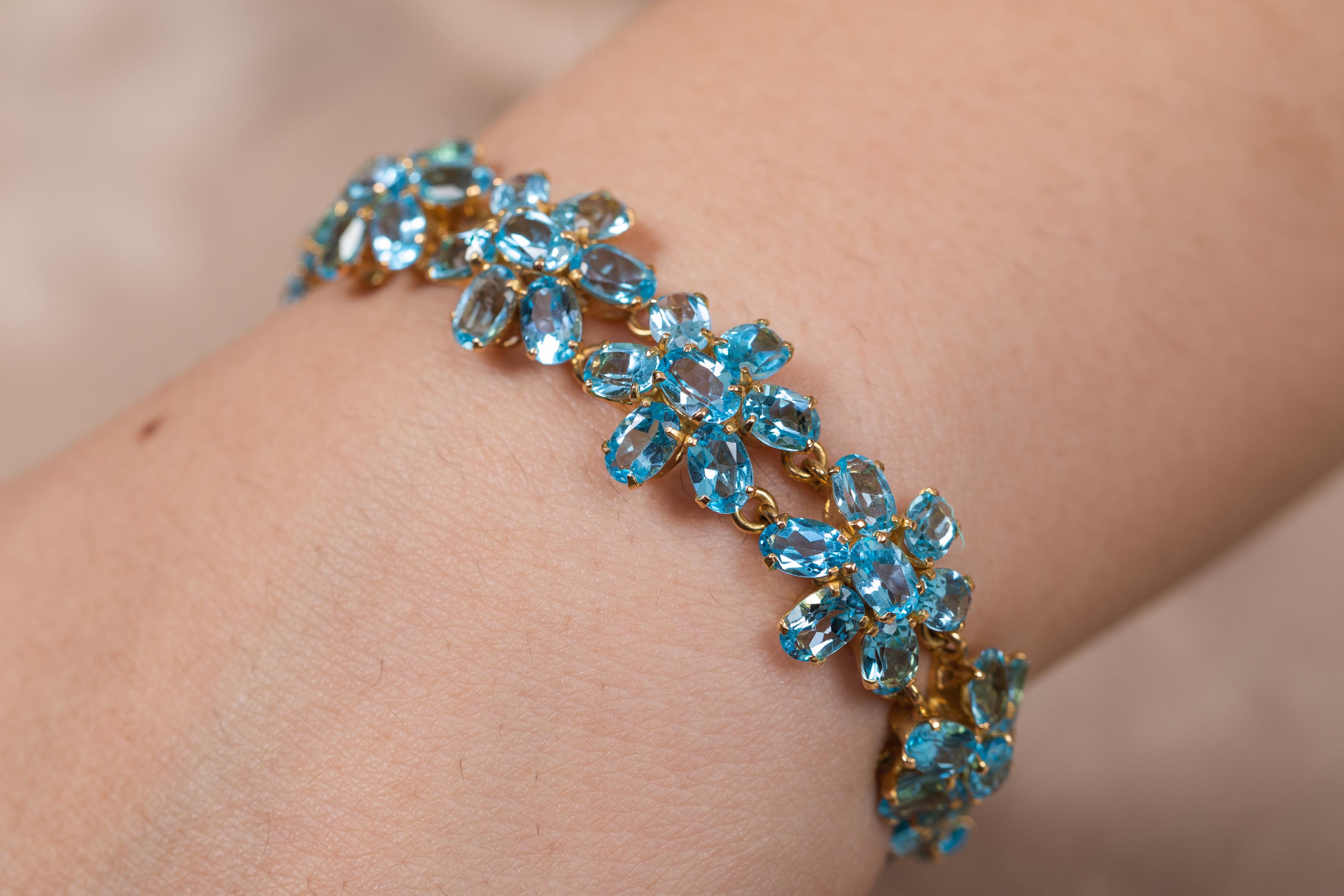 This Blue Topaz Floral Bracelet in 18K gold showcases 77 endlessly sparkling natural blue topaz, weighing 38.1 carats. It measures 7.5 inches long in length. 
Topaz improves communication and expression. 
Designed with perfect oval cut blue topaz