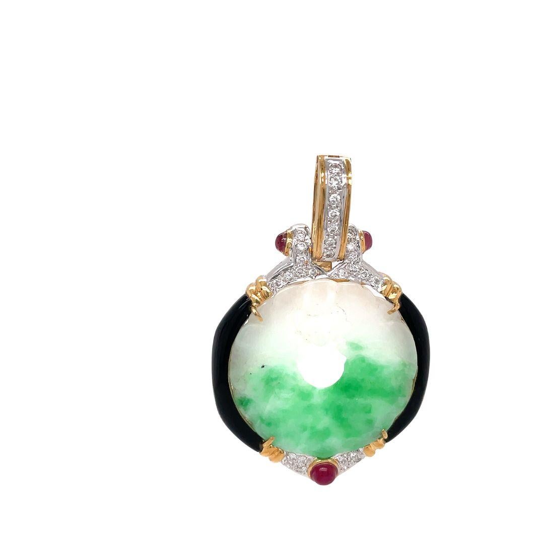 This gorgeous pendant features a round-shaped plaque of hand-carved jade with an ornate cut-out design, onyx, hinged clip bail decorated with diamonds accented with 2 cabochon rubies, one on each side of the bail crafted in 18k yellow gold. 

The