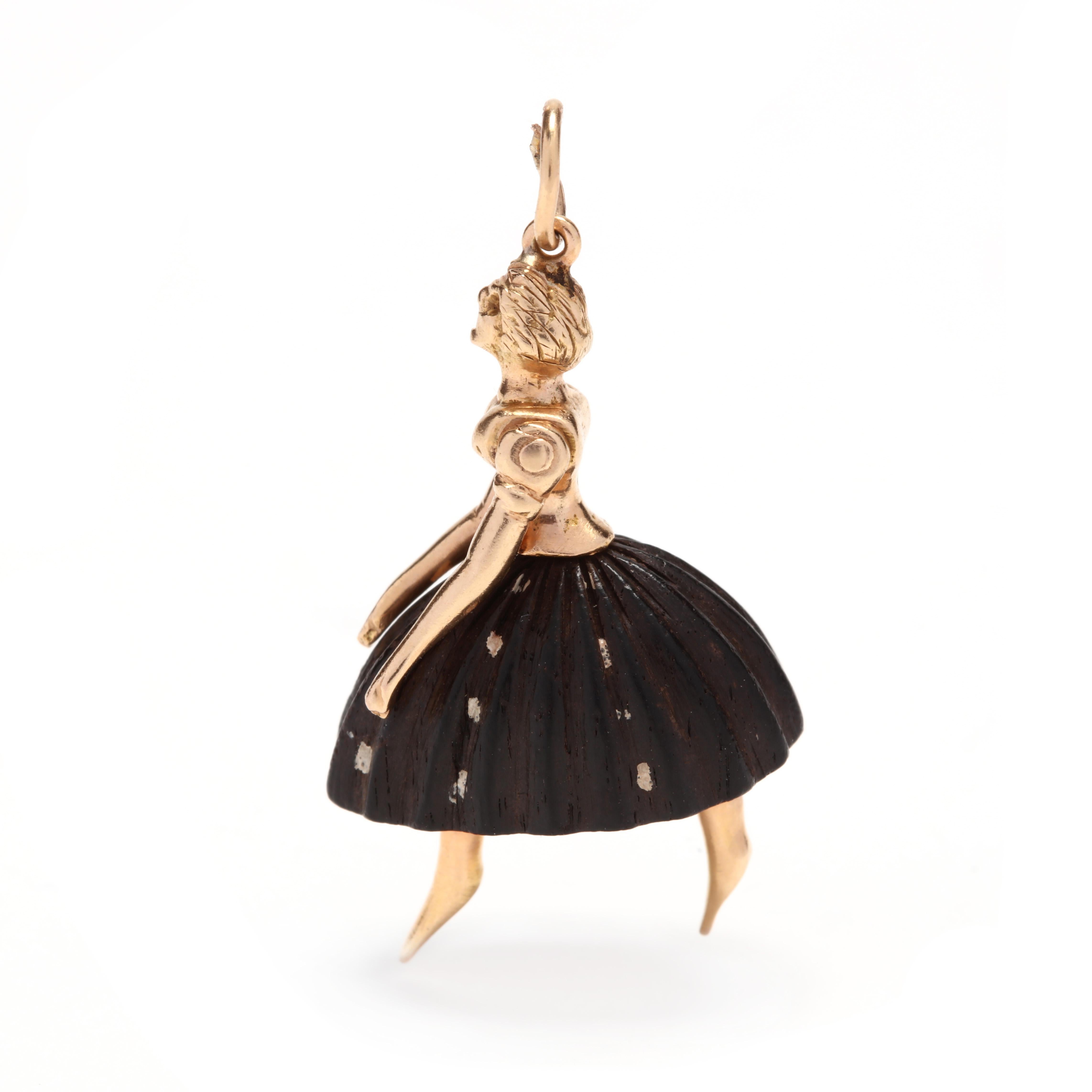 An 18 karat yellow  gold and carved wood ballerina charm / pendant. This pendant features a female ballerina motif with a carved wooden skirt and articulated arms.

Length: 1 3/8 in.

Width: 3/4 in.

3.58 dwts.

* Please note that this is a vintage