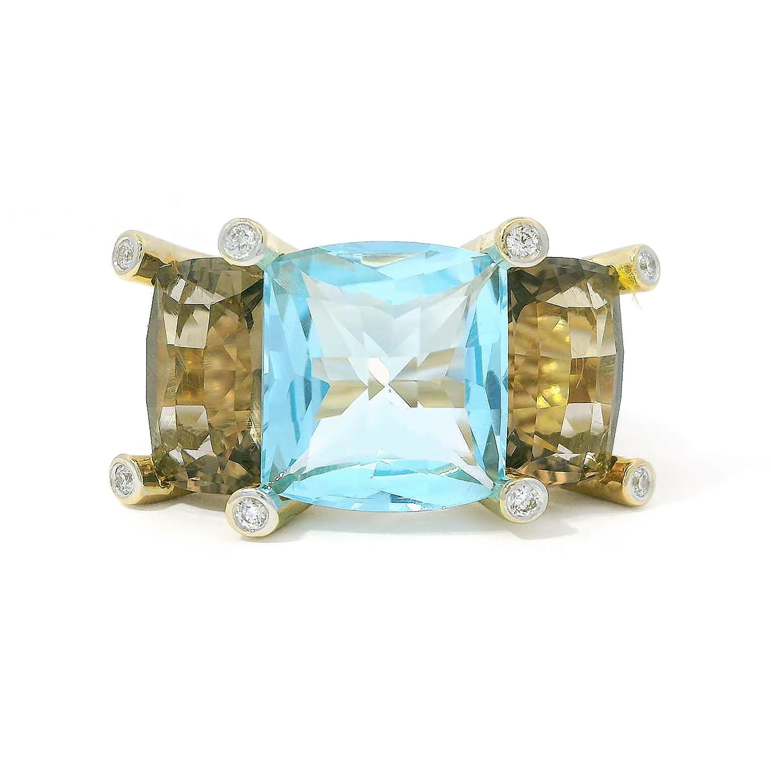 Earth tones are the vivid basis of this blue and brown topaz ring. A cushion cut of blue topaz flickers with radiance in the center of the ring, with a cushion cut of translucent brown topaz on each side. 18k yellow gold prongs feature a brilliant