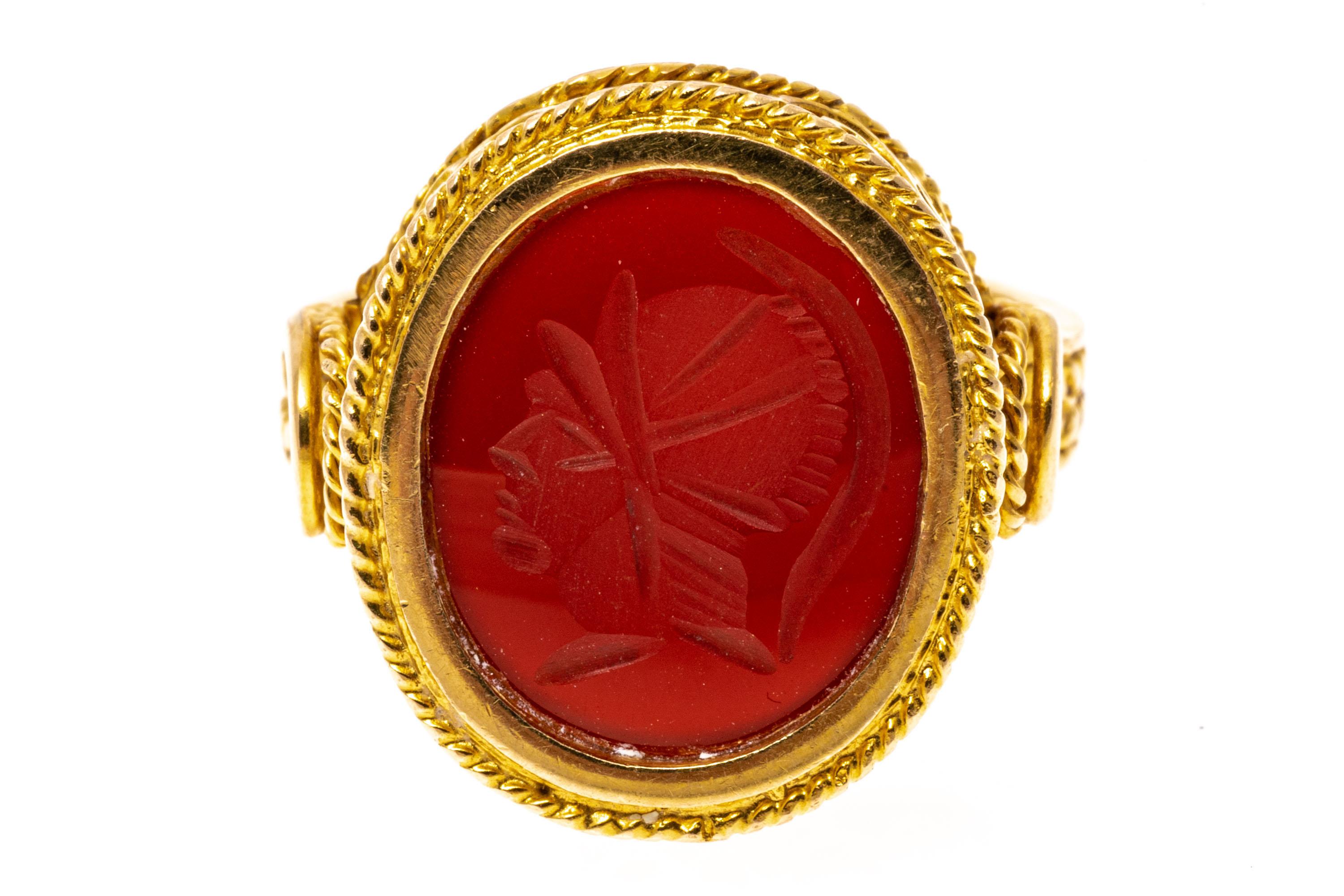 18k yellow gold ring. This attractive contemporary oval carnelian intaglio ring has a handsome figure of a soldier, facing to the left. The ring is also adorned with a braided pattern on the frame and shank, and an ornate scrolled gallery.
Marks: