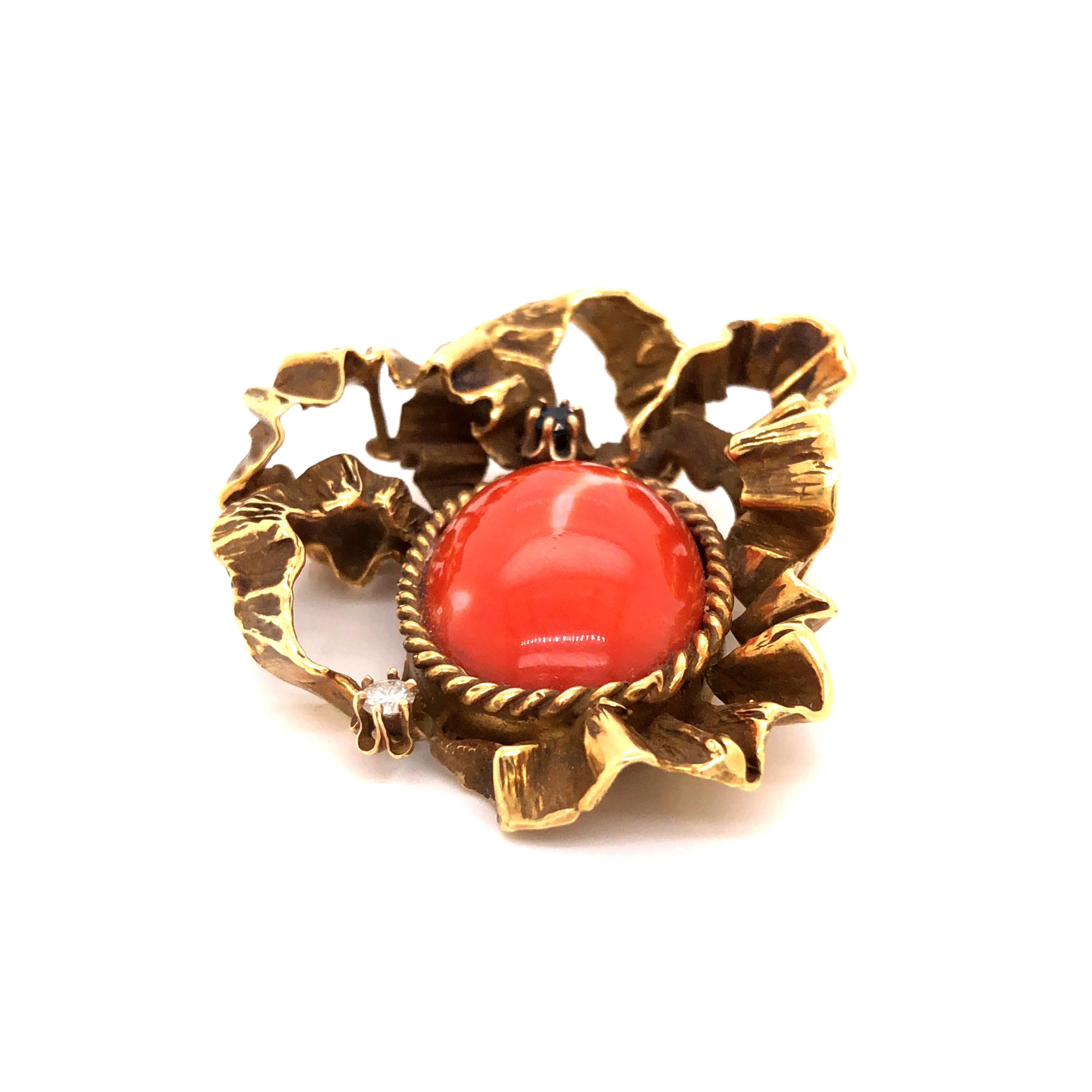 An 18K yellow gold brooch pendant featuring an oval cut coral cabochon with a single round brilliant cut diamond accent and a single cut faceted sapphire.

Stone: Coral, Diamond, Sapphire

Metal: 18K Yellow Gold

Size: 1.70