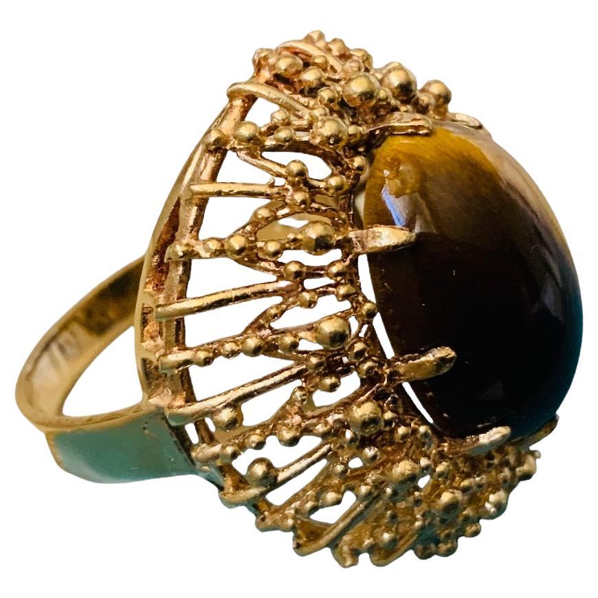 This is a 18K yellow gold and Tiger Eye cocktail ring. It depicts an oval shaped cabochon Tiger Eye stone mounted in gold prong setting and surrounded by a wreath made of spikes with tiny beads. The Tiger Eye’s width and length is 0.5 and 0.75