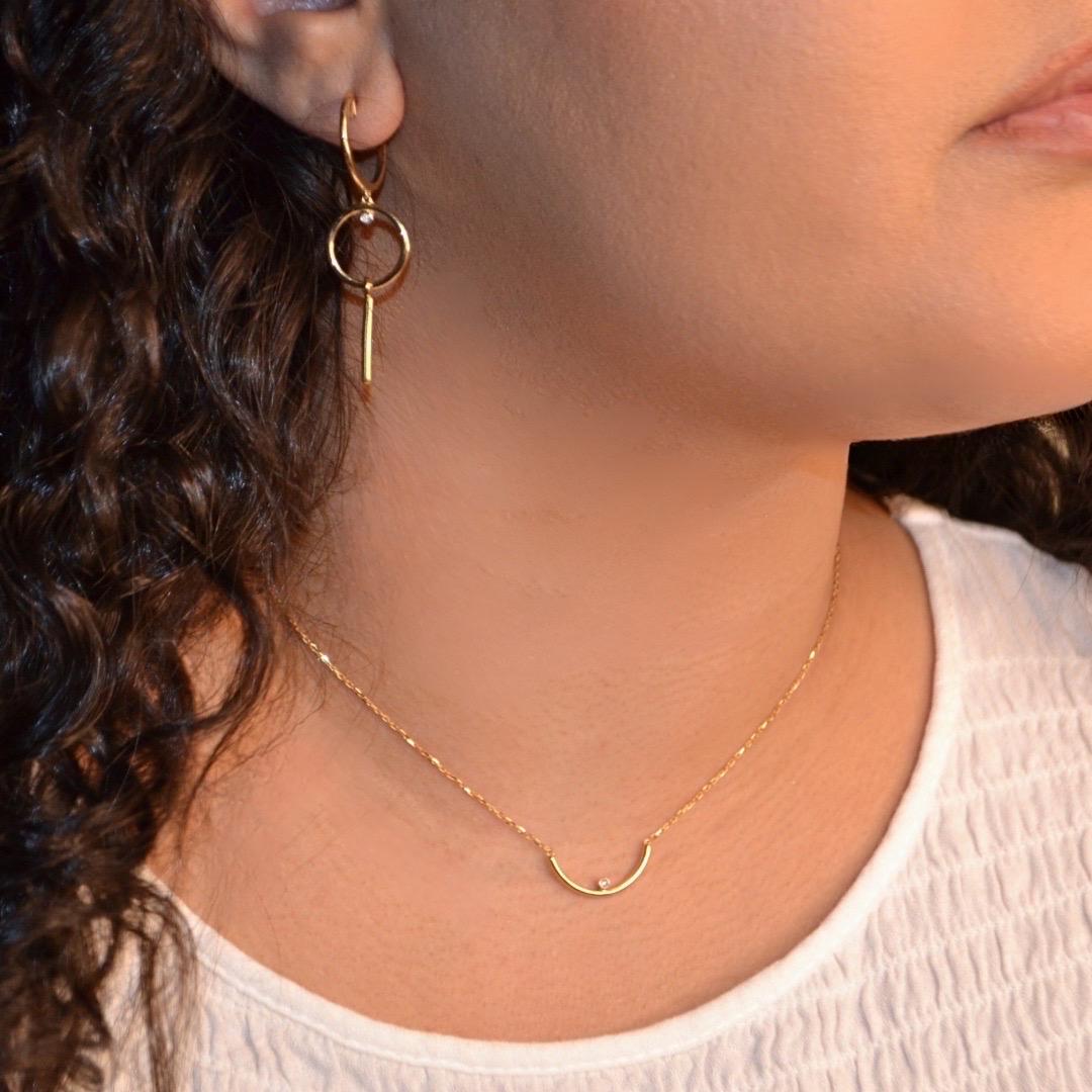 This elegant 18K yellow gold necklace features a sleek crescent-shaped pendant, beautifully complemented by a single diamond accent set at the center. The minimalist design creates a modern yet timeless piece, perfect for everyday wear or as a