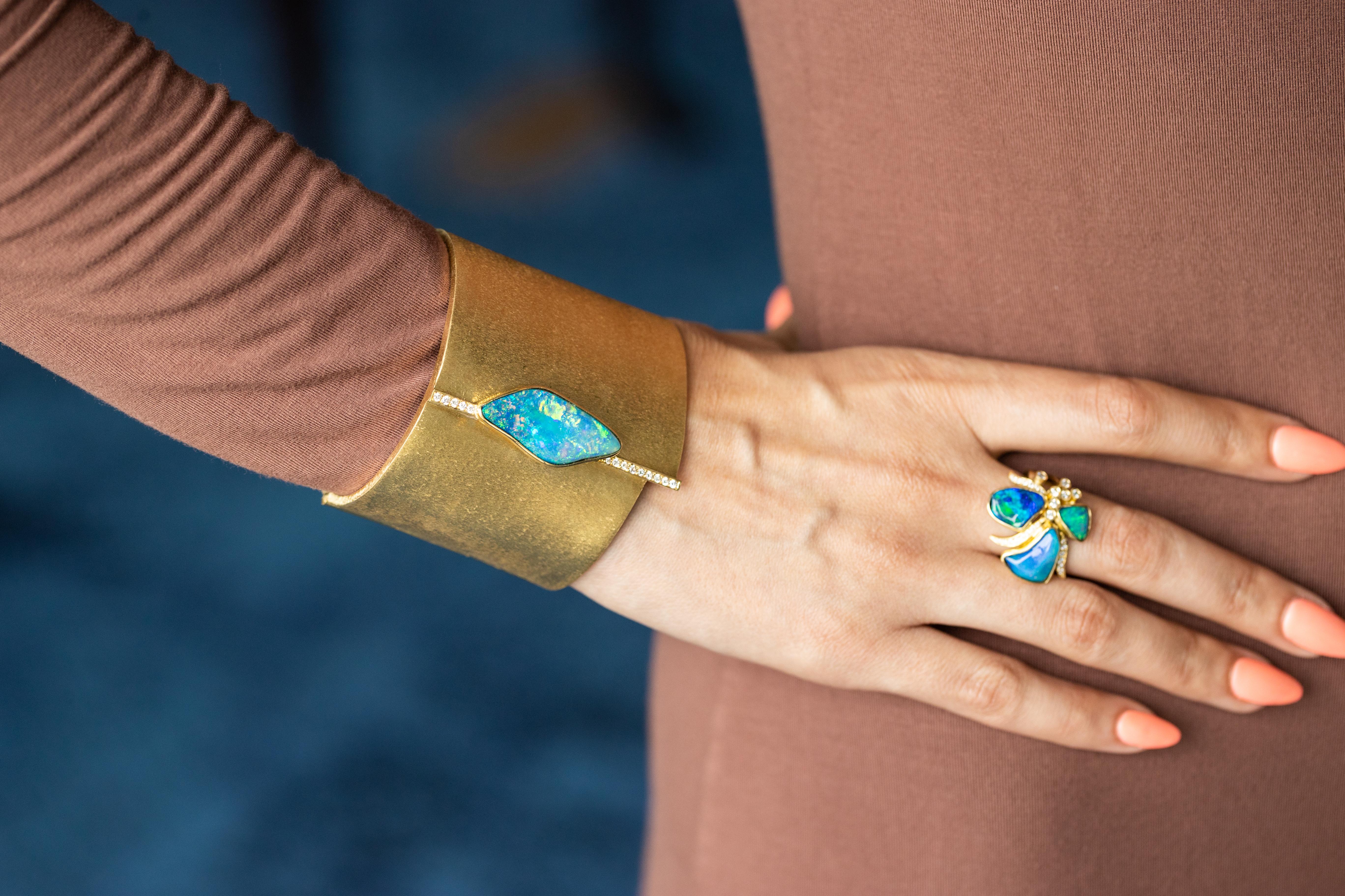 Élevez votre élégance avec ce bracelet manchette envoûtant, qui témoigne de la maîtrise artistique de Ruth Grieco. En son cœur se trouve un captivant doublet d'opale bleue de 12,30 carats, une pierre précieuse connue pour son jeu enchanteur de