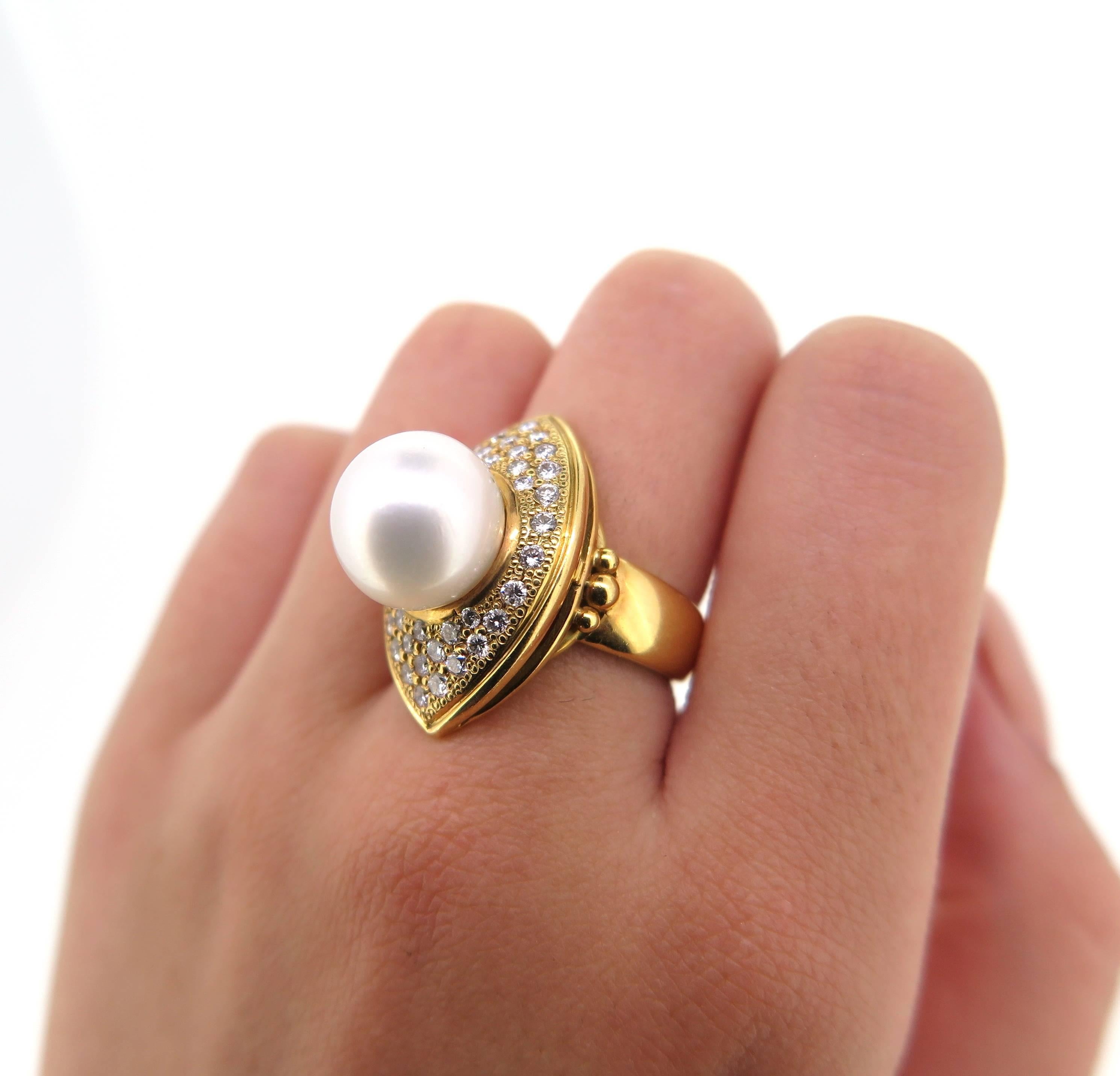 Featuring an 18 Karat yellow gold modern dress ring with a marquise shaped top plate. The ring is set with a 11.8 mm uniform round cultured south sea pearl. the peal is surrounded by 38 graduated modern Round Brilliant Cut Diamonds. The ring has a