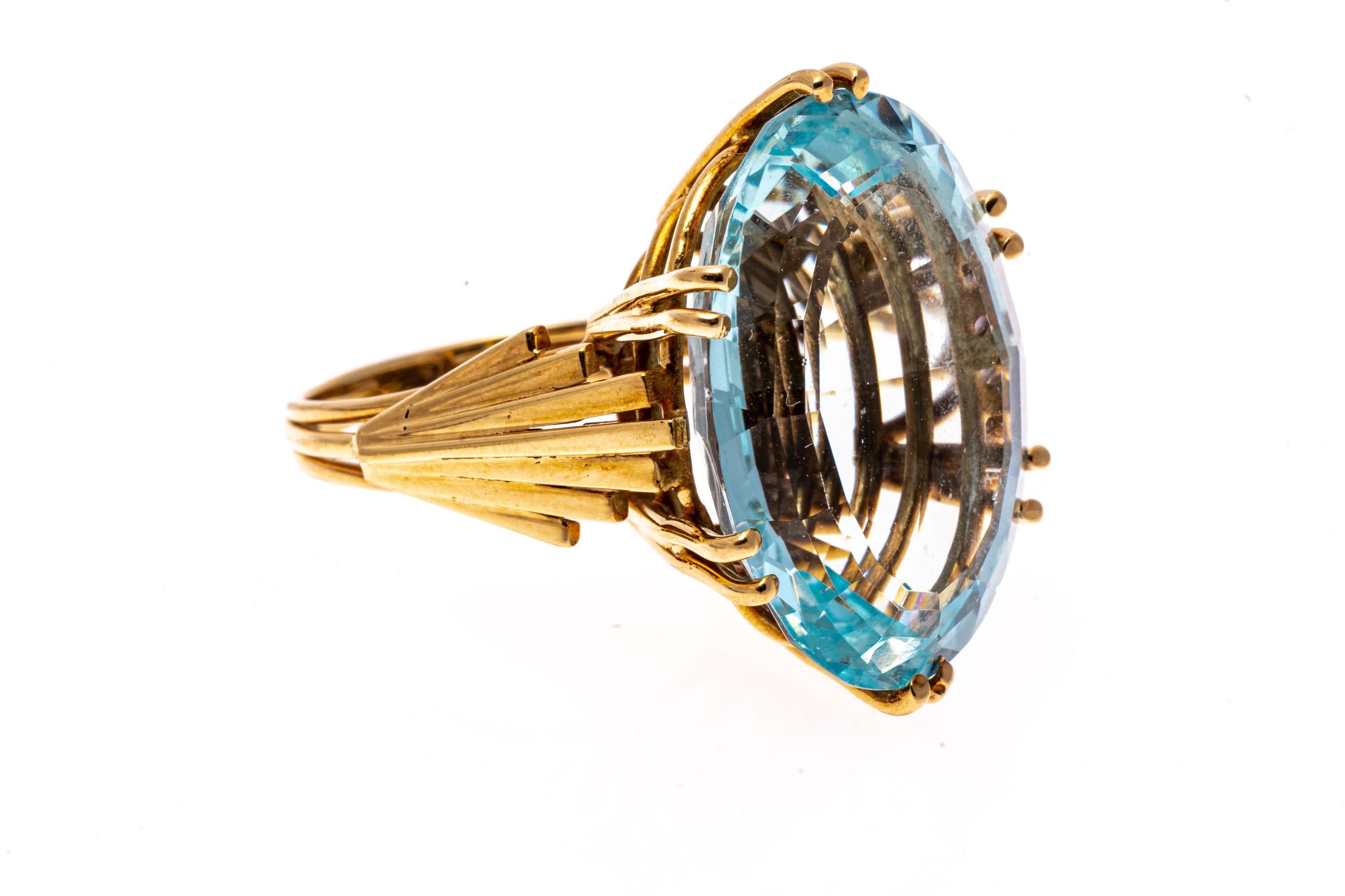 18k yellow gold ring. This elegant ring has a very retro look, with a large center oval cut, pale blue color aquamarine, approximately 16.36 CTS. The center stone is set with six split prongs, and is decorated with Deco-style fan shoulders which