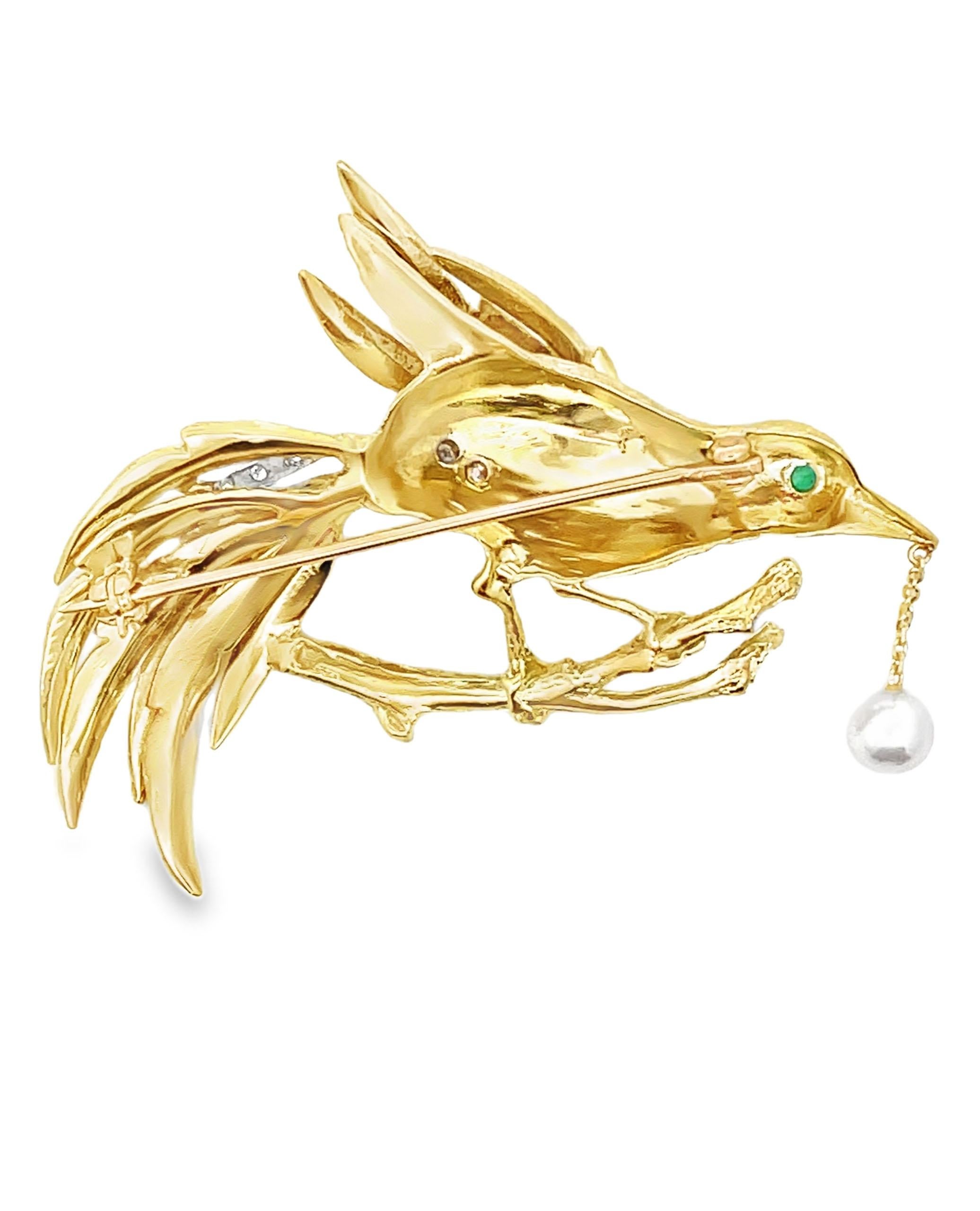 18K yellow gold bird brooch with 13 round faceted diamonds weighing approximately 0.30 carat and one round faceted emerald weighing approximately  0.15 carat. Dangling from the bird beak is a cultured pearl measuring at  5.7mm.

- Total weight 21.50