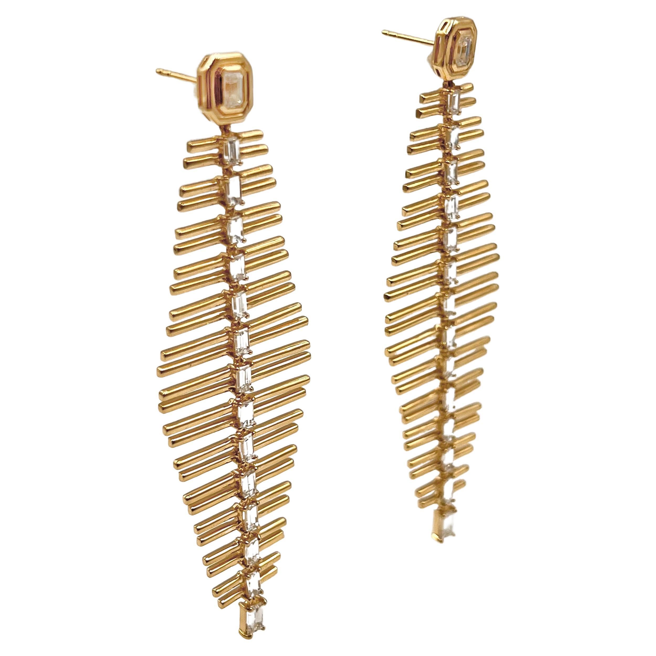 Stylized fishbone long drop earrings in polished 18k yellow gold.  Tops are each bezel-set with an emerald-cut diamond with an additional fourteen baguette-cut diamonds running down the center of either earring. Thirty diamonds weighing 3.68 total