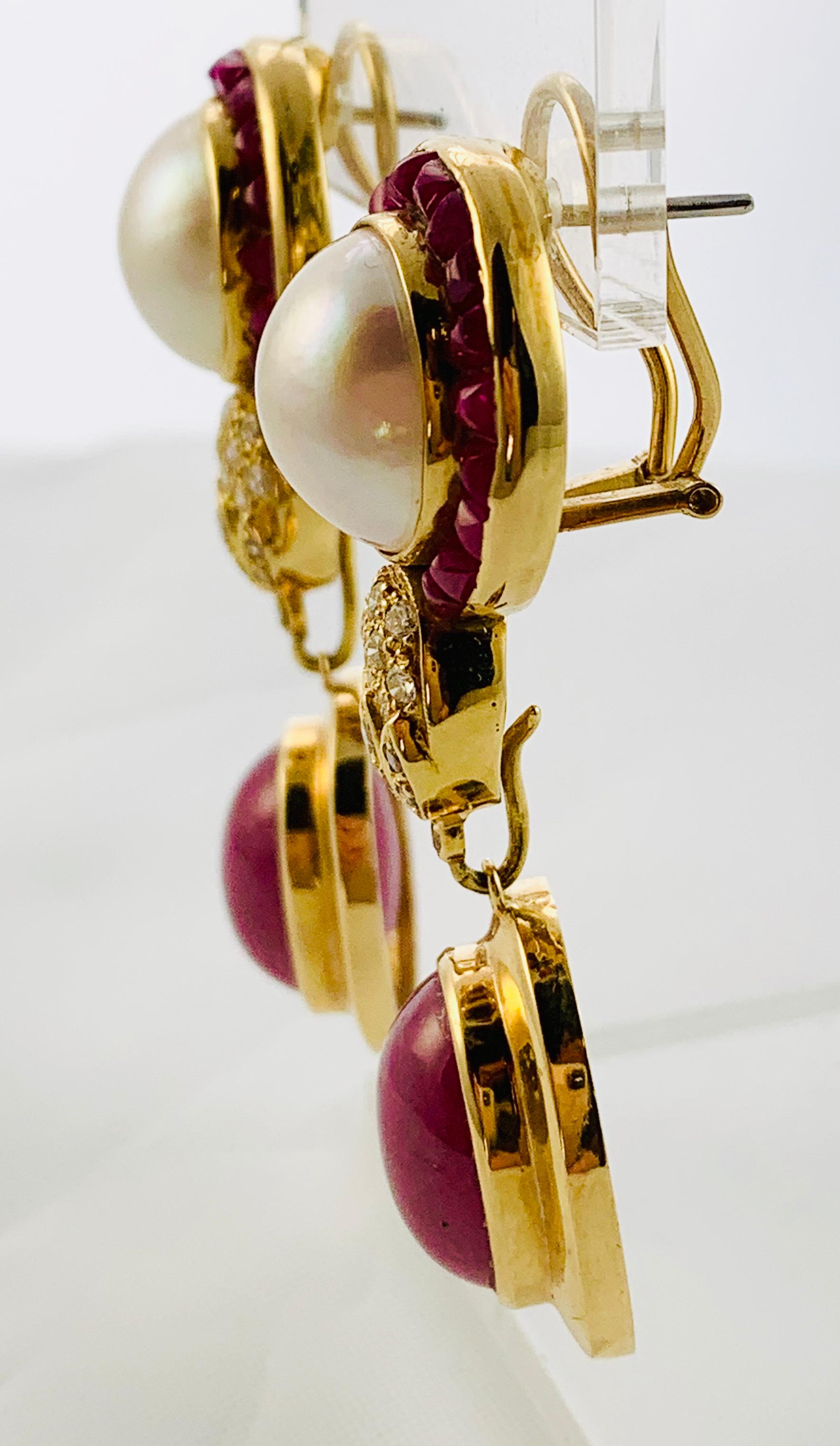 Gorgeous Drop Earrings!!! Made in 18K yellow Gold, they have three tiers. The top tier features  a 14mm Mobe Pearl That is surrounded by Calibre Cut Rubies. The middle connector tier has 17 round diamonds. The bottom, removable dangle features  a