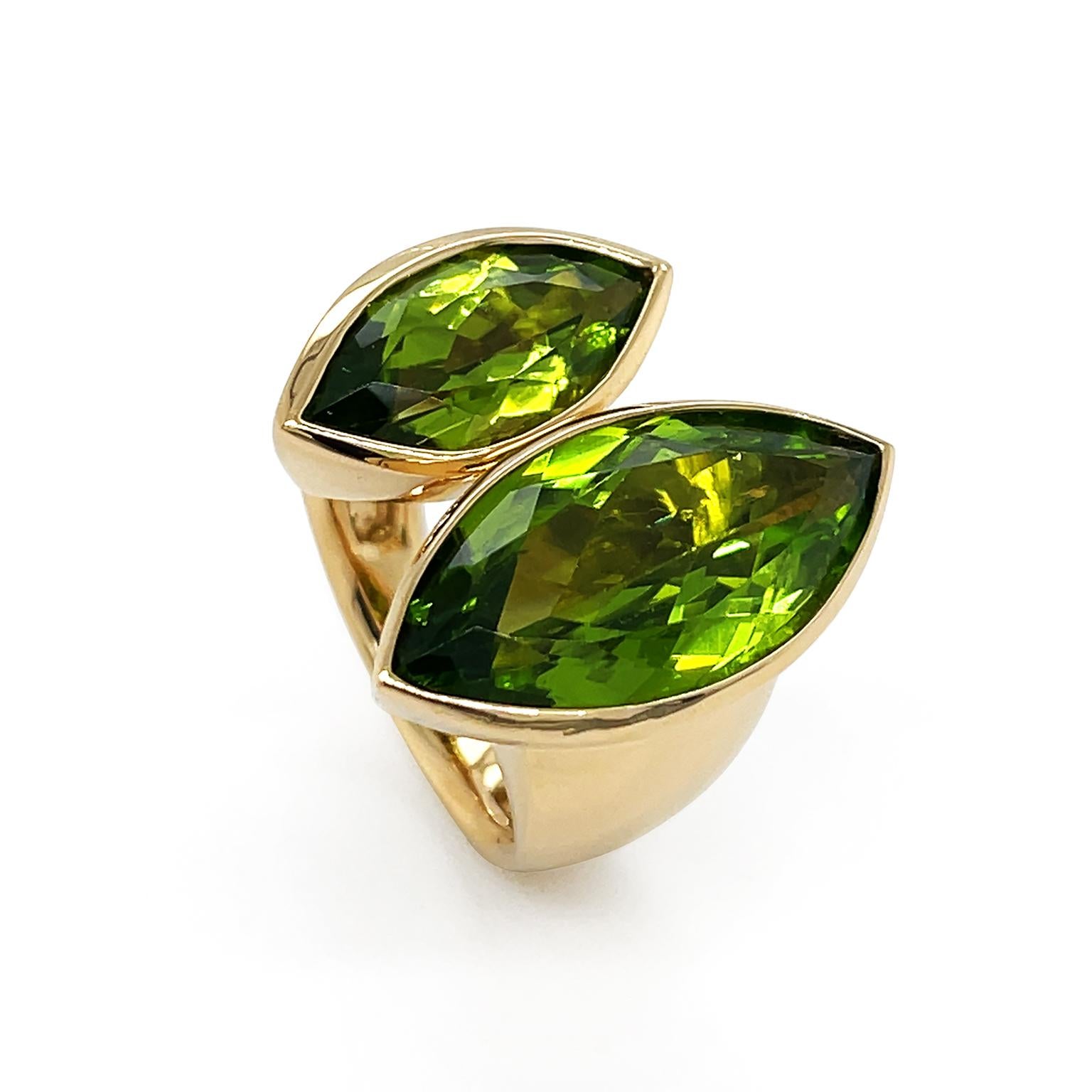 The symmetrical poise of the marquise shape is presented with peridot as the gemstone of choice for this 18k yellow gold ring. One side of the band features a small bezel-set peridot, while the other features a bezel-set peridot. Both gemstones meet