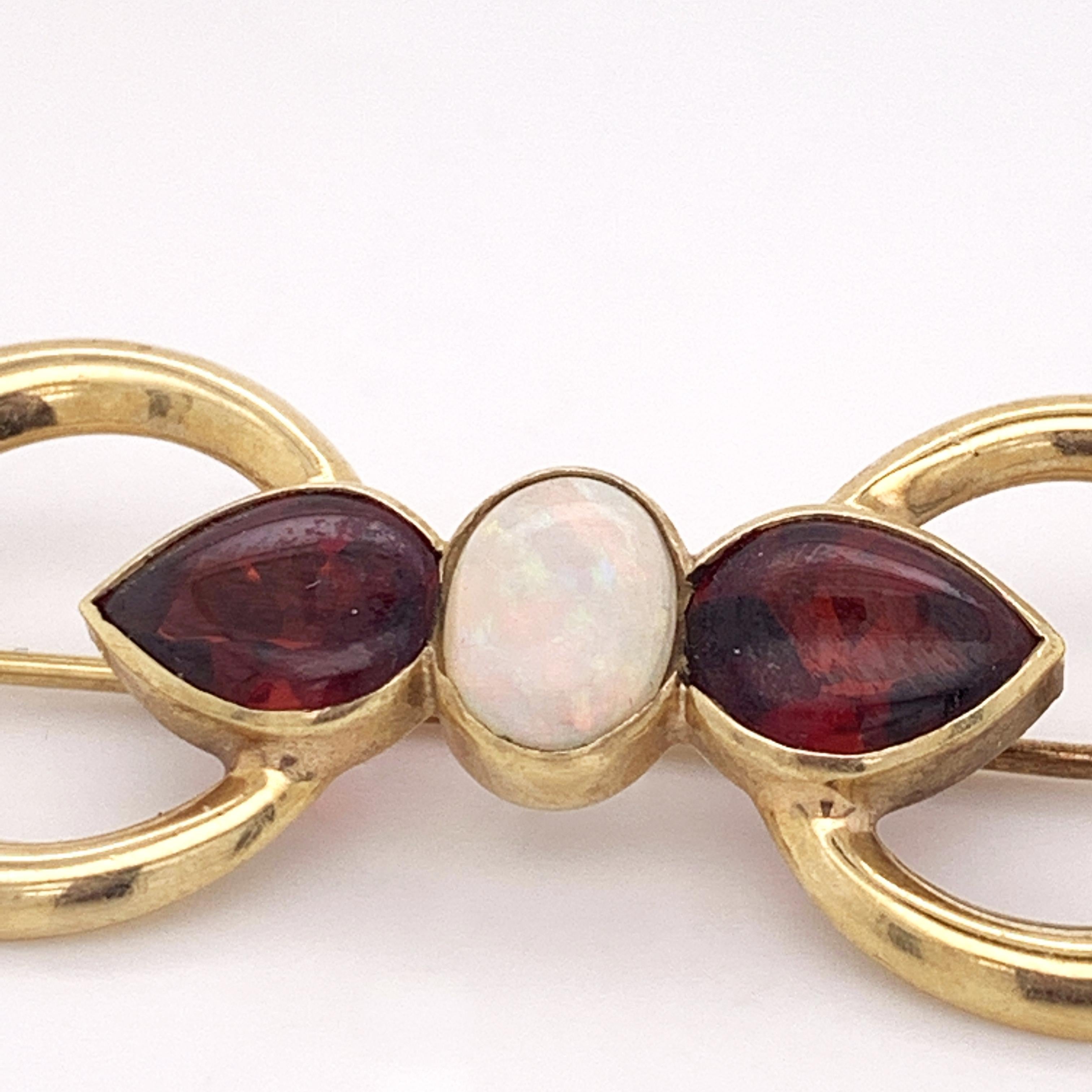 Here we have an stunning 18K yellow gold brooch featuring a beautiful oval shaped NaturalOpal flanked by two lovely deep red pear shaped Almandite Garnets. The lustrous loops of yellow gold are perfectly juxtaposed against the gems which allows both