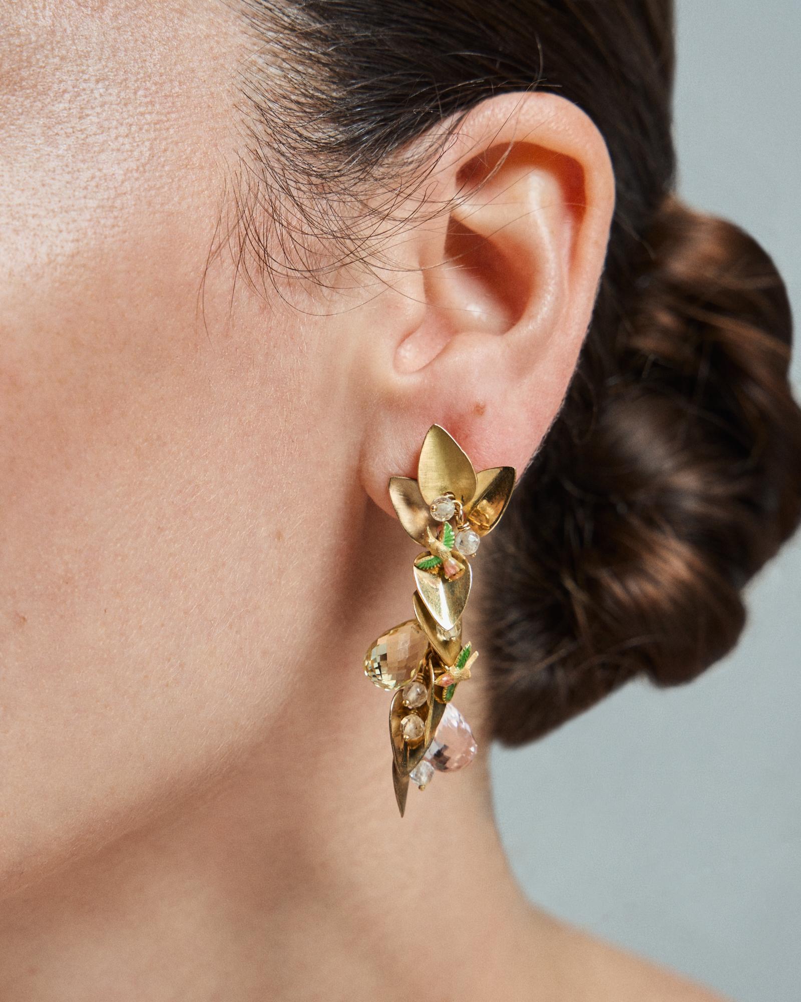 18k Yellow Gold Earrings with Fire Enamel Beryls Rock Crystal Hummingbird Motif

Crafted in 18k yellow gold, these extraordinary earrings evoke the charm of a lush, hanging garden. Golden leaves cascade gracefully, embracing faceted beryls of