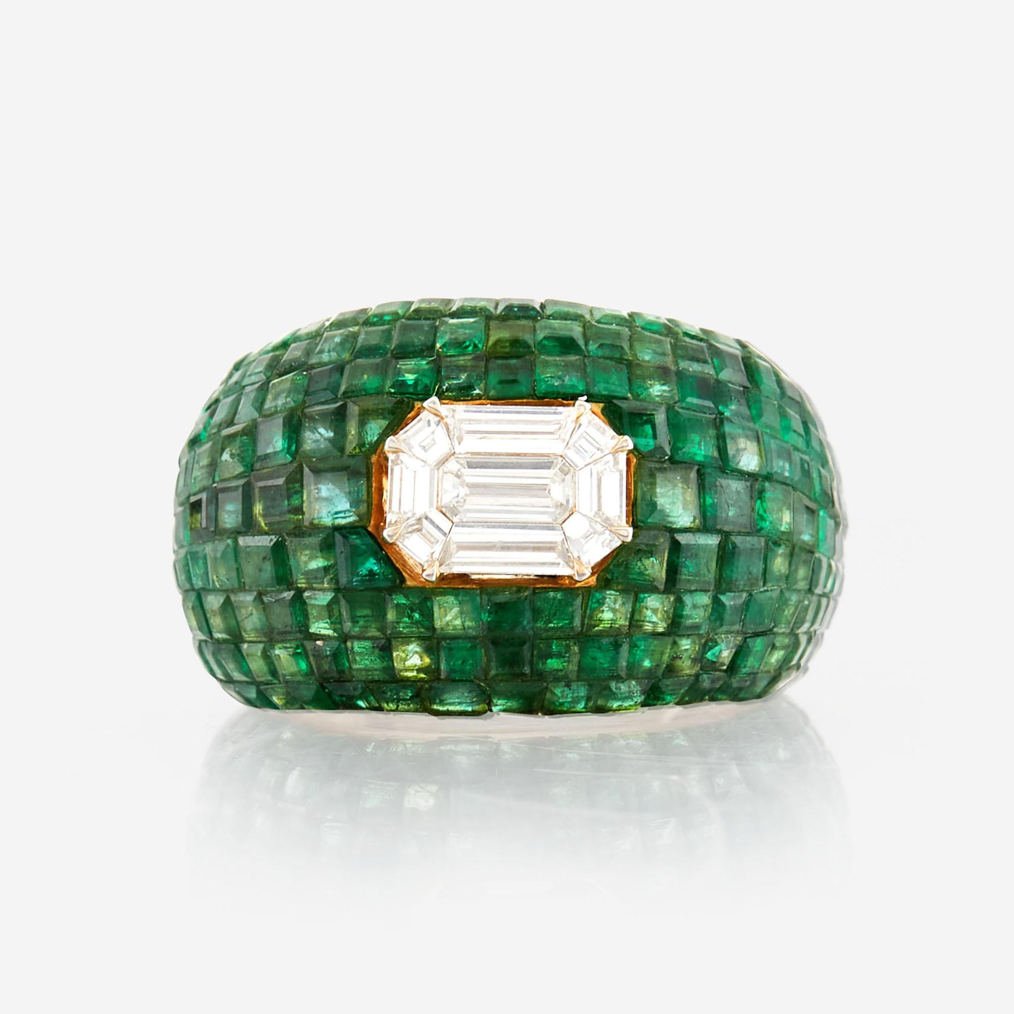 This stunning 18K yellow gold bombe ring features a sparkling pie cut diamond, surrounded by beautiful invisibly set emeralds. The total weight of the emeralds is an impressive 6.6 carats, while the center diamonds weigh in at 0.7 carats. The