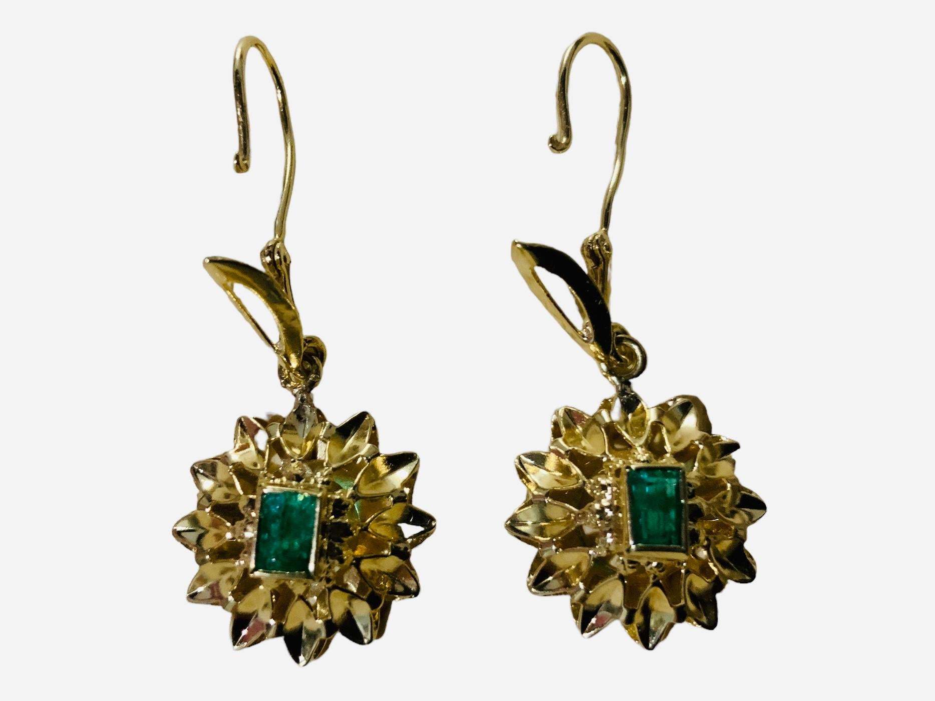 This is a Pair of 18K yellow gold Emerald Drops Earrings. The emerald cut tiny emeralds are in bezel setting and mounted in 18K yellow gold. A gold wreath of leaves adorns the back of the mounted emeralds. Both earrings are hallmarked 18K. They are