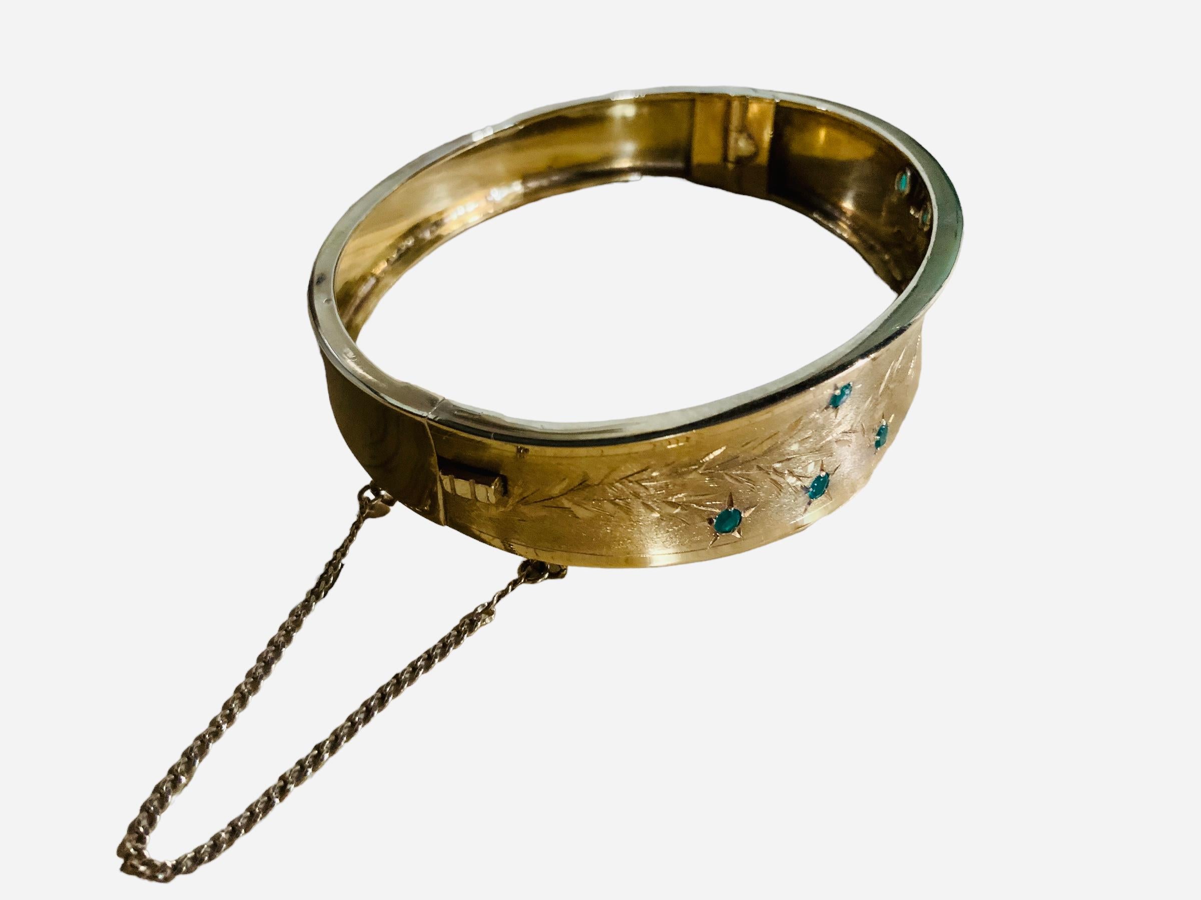 This is an 18K yellow gold and emerald hinged wide bangle. Two long engraved branches adorned with eight pave round cut emeralds of approximately 0.22 ct enhance the bangle. A push button barrel clasp close/open the bangle. It is hallmarked 18K in