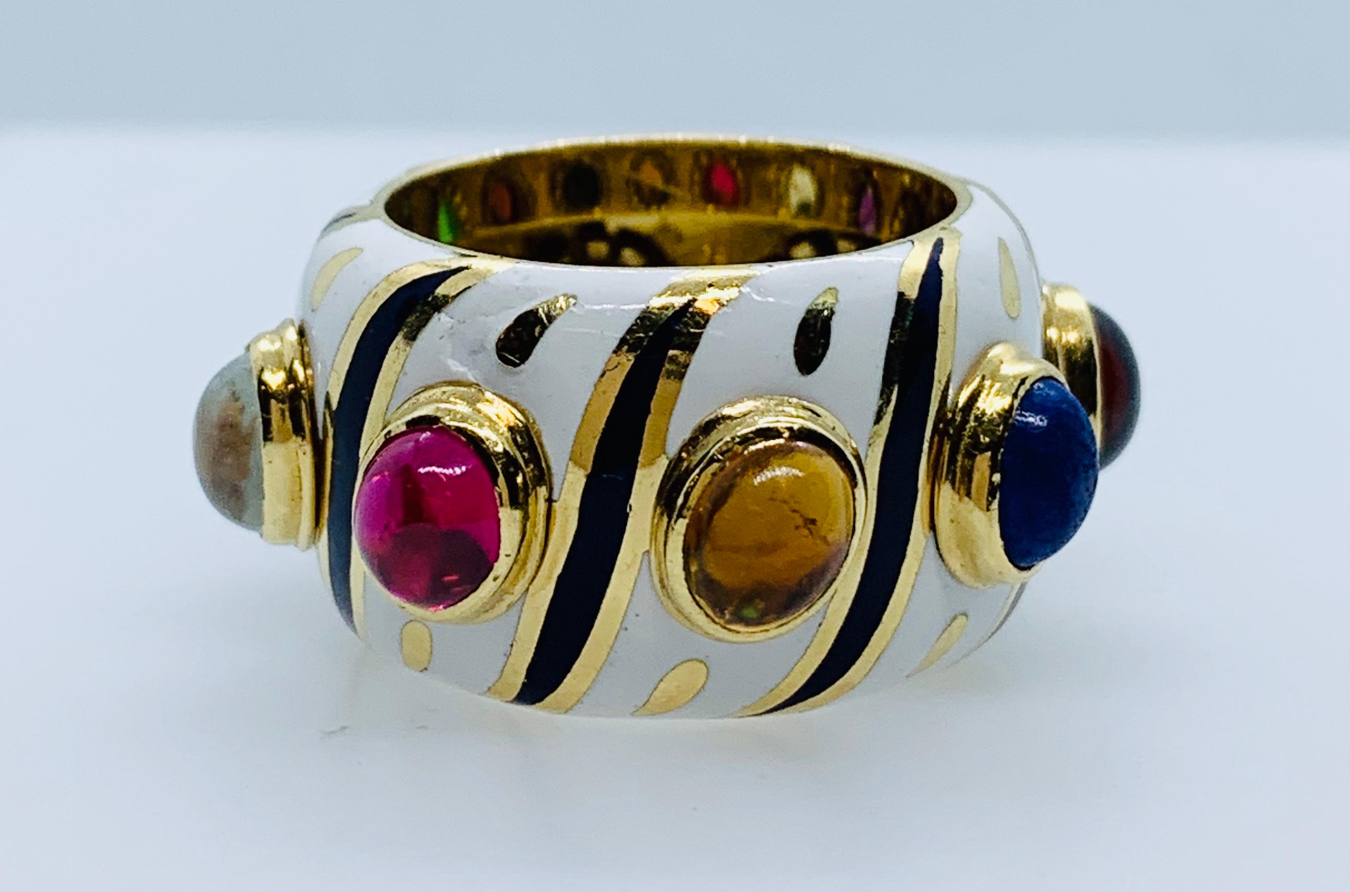 What a gorgeous and unique band ring! This piece is made in 18k yellow Gold that is covered in white and black enamel. There are 8 bezel set, cabochon cut gemstones. Stone colors are blue, red, green, tiger eye, purple, clear, pink & amber. This