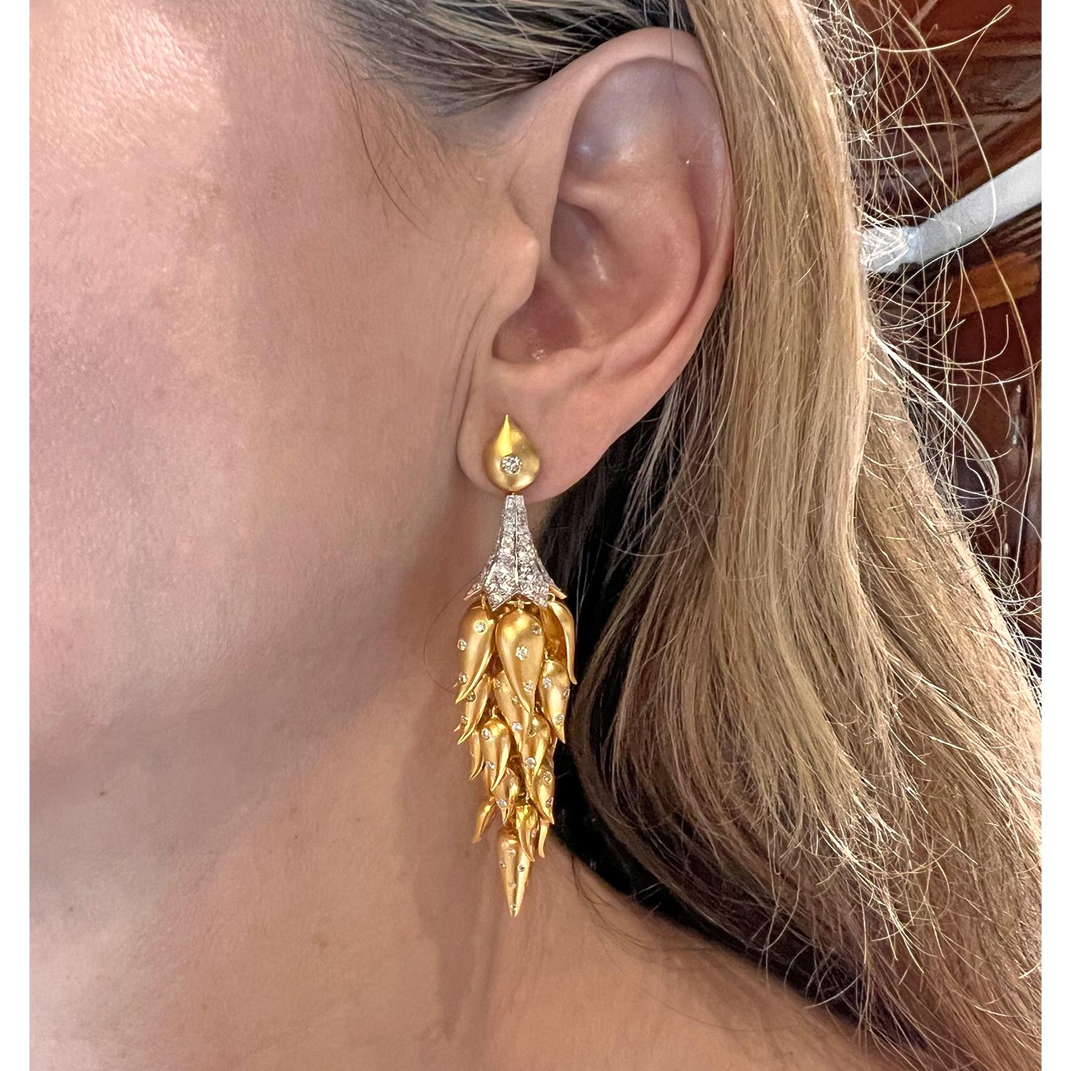 Longues boucles d'oreilles en forme de goutte, présentant une cascade de feuilles tombantes en or jaune 18k, chacune accentuée par de petits diamants ronds de taille brillant. Les feuilles sont suspendues à une monture en or jaune 18k en forme de