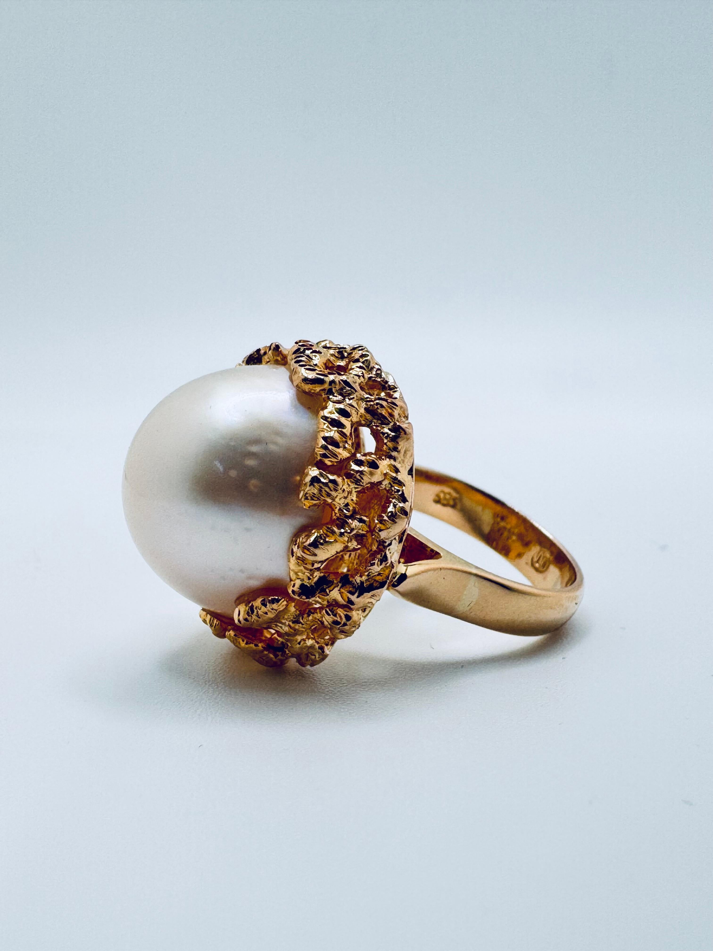Réalisée en luxueux or jaune 18 carats, cette bague distinctive met en valeur une magnifique perle Mabe ronde de couleur crème de 16,5 mm comme pièce maîtresse. Le lustre doux de la perle est mis en valeur par un sertissage unique de style libre,