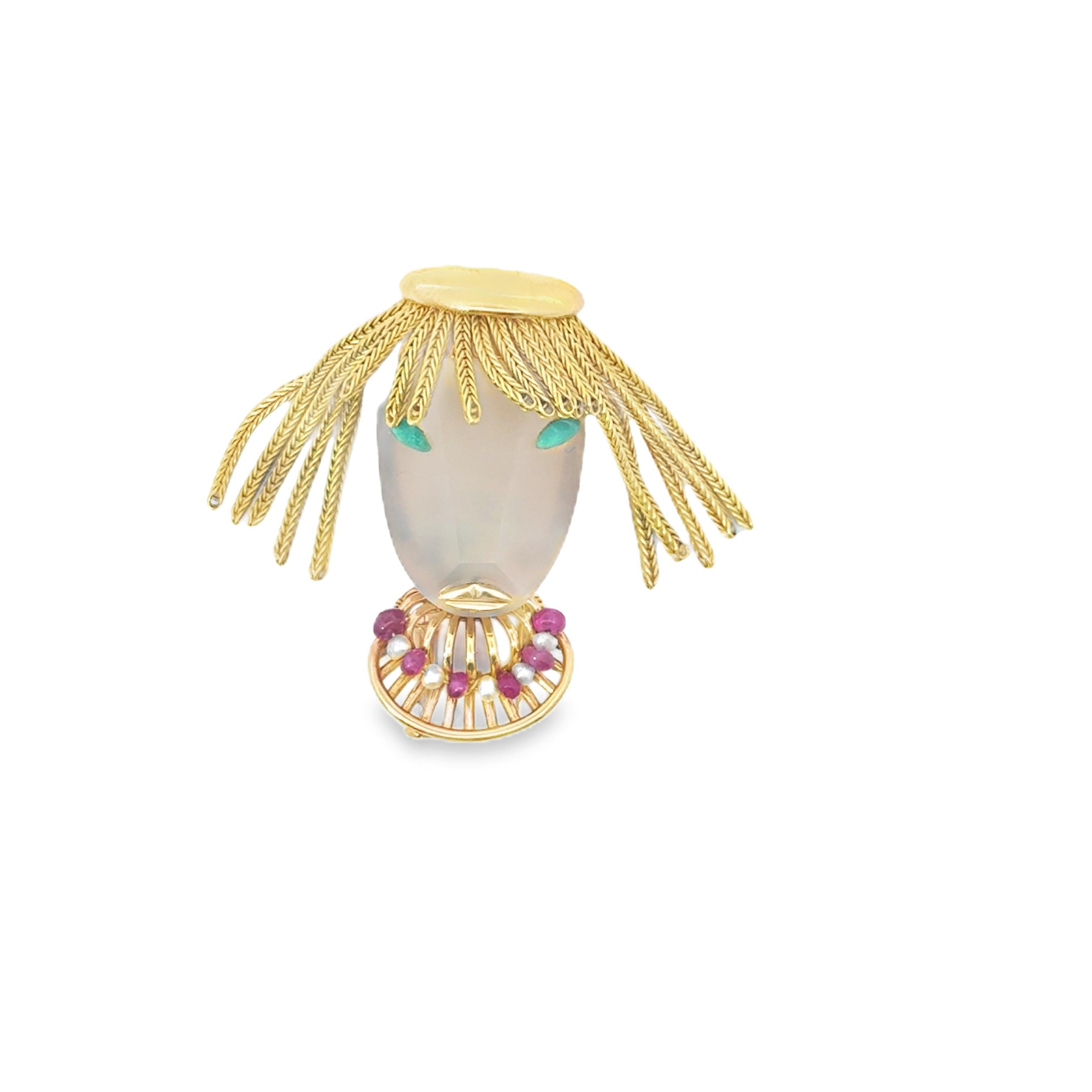 This unique brooch representing a woman face, highlighted by a central crystal face with emerald accents. The intricate gold detailing forms a striking headdress, adding a touch of whimsy to the piece.

Crafted in 18k yellow gold, the brooch is