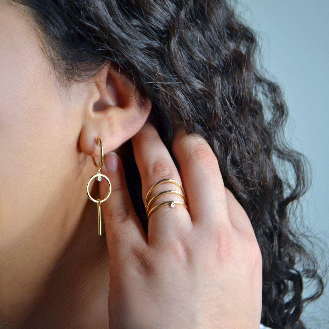 Questi moderni orecchini a goccia geometrici in oro giallo 18 carati presentano un design elegante e minimalista. Gli orecchini sono composti da un cerchio aperto e da una barra verticale, creando un look chic e contemporaneo. Un piccolo diamante