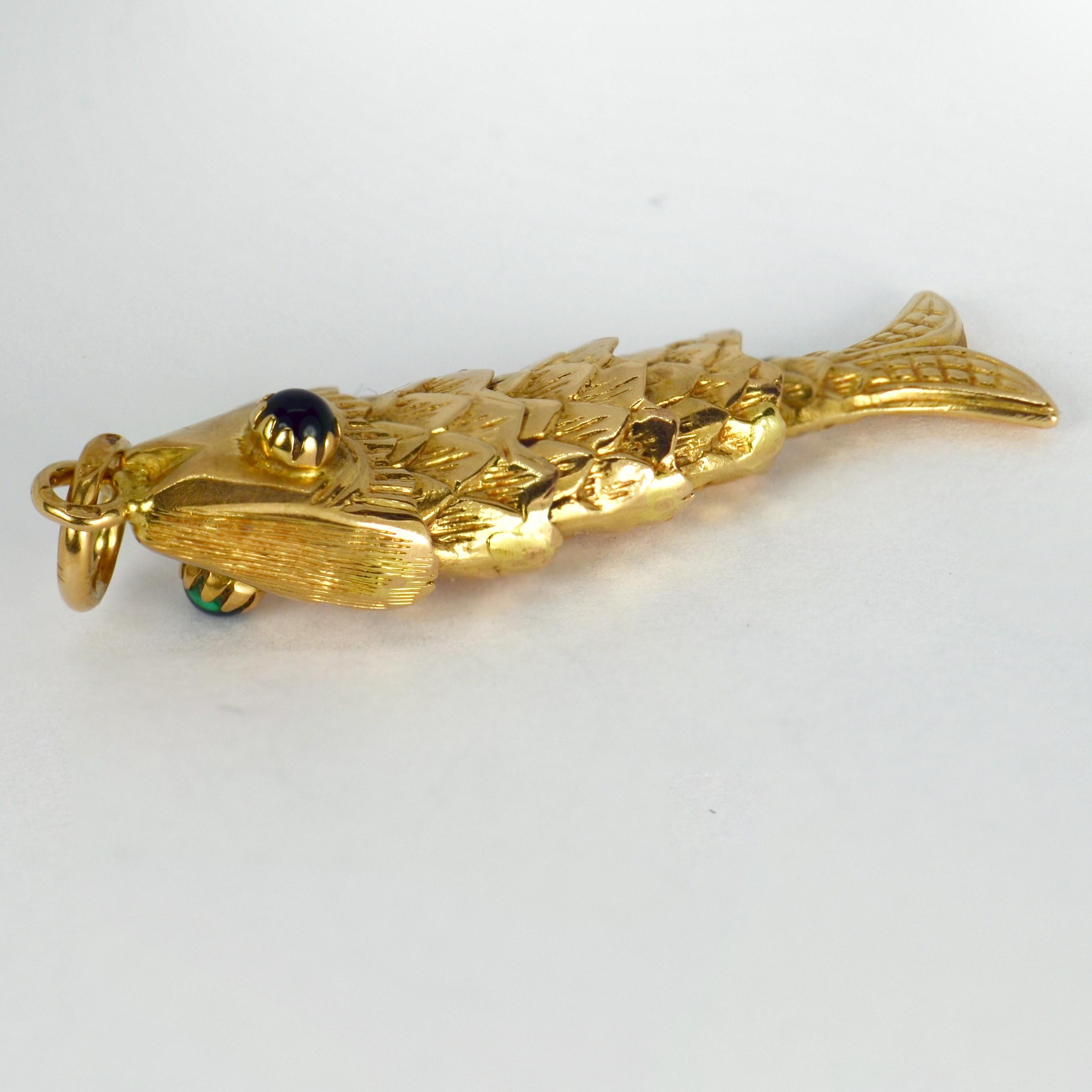 A large 18 karat (18K) yellow gold charm pendant designed as an articulated fish with foiled green paste eyes. Stamped with French import marks and 750 for 18 karat gold.

Dimensions: 4.3 x 1.05 x 1 cm (not including jump ring)
Weight: 4.79 grams
