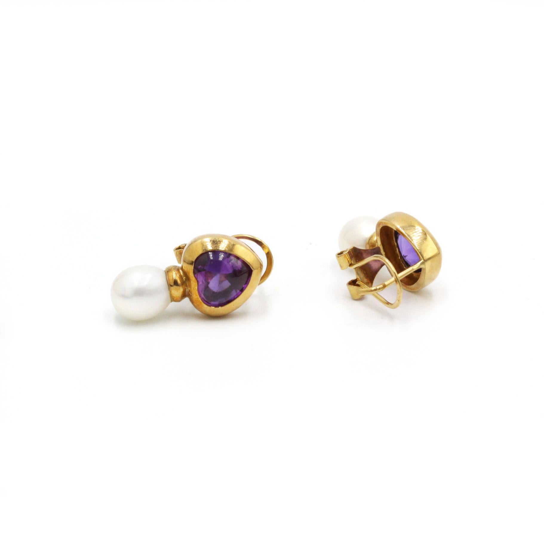 Ces charmantes boucles d'oreilles associent l'éclat violet profond des améthystes en forme de cœur à la chaleur lustrée des perles de culture classiques. Chaque boucle d'oreille est ornée d'une améthyste facettée, sertie en chaton et sculptée en un