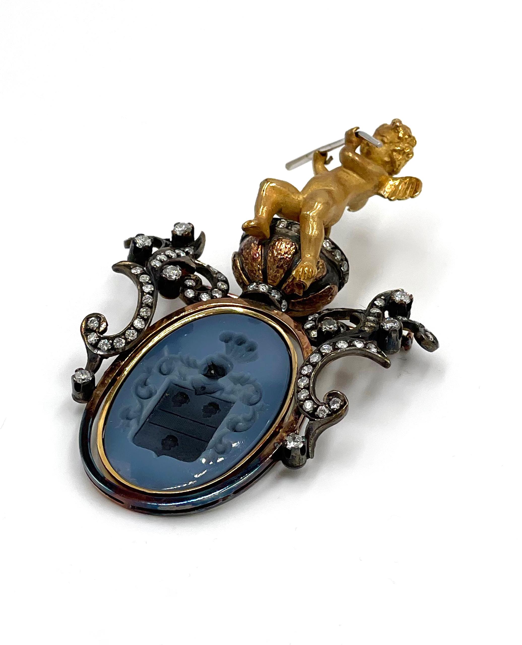 Pre owned vintage estate 18K yellow gold Intaglio and diamond brooch/pendant.  The brooch has a large full figured cherub at the top that is seated on an urn set with diamonds.  The oval frame below swivels and is bezel set with a blue/gray hard