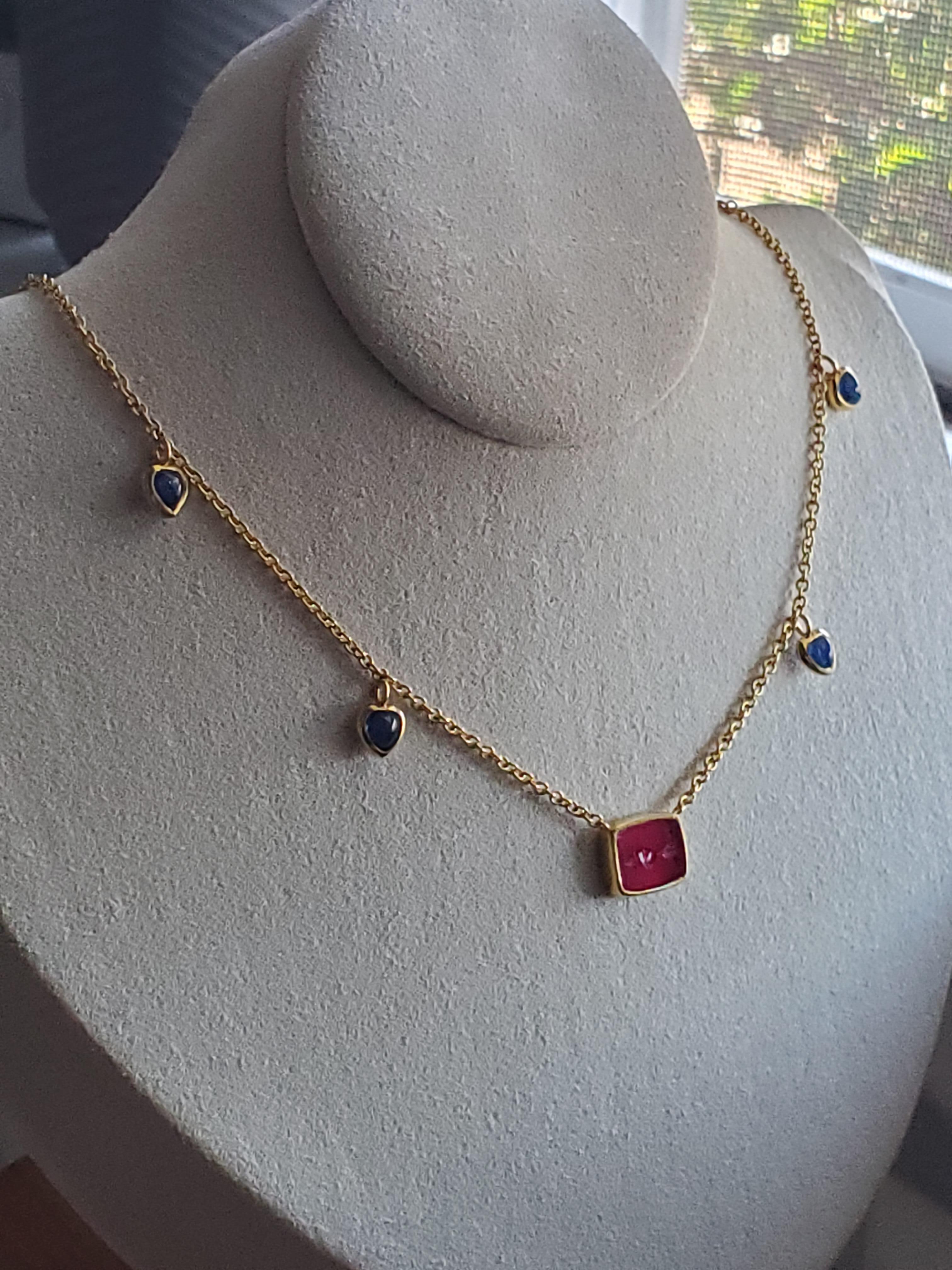 Notre collier en or 18 carats pr�ésente une tablette de rubis de laboratoire avec une intaille de cœur et de flèche sculptée à la main, qui brille d'un rose profond. Quatre cœurs de saphir naturel en cabochon, sertis, entourent le rubis, ajoutant à