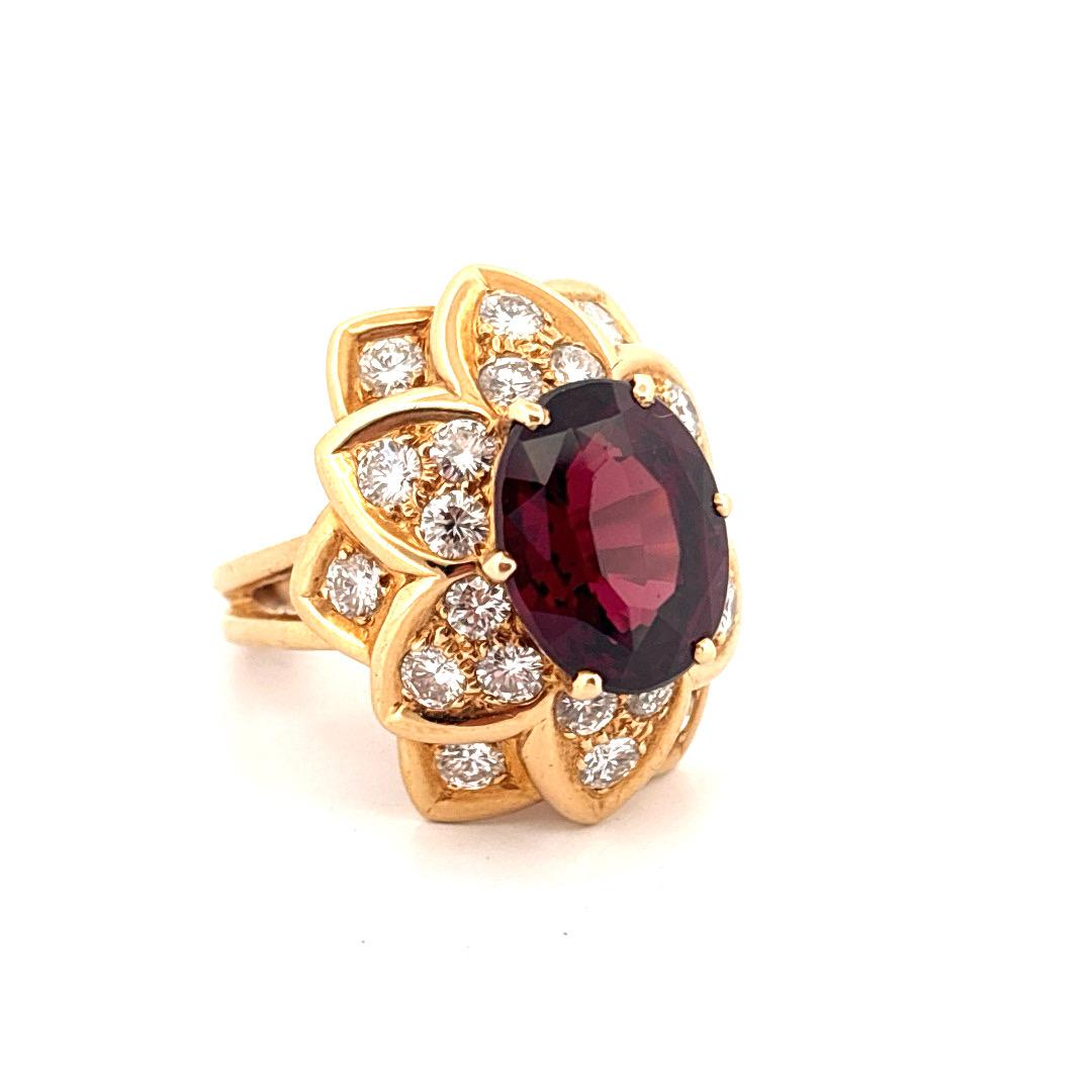 Cette magnifique bague en or jaune 18 carats présente en son centre un grenat de 7,00 carats, taillé en ovale, qui irradie des teintes cramoisies profondes avec une profondeur et une brillance hypnotiques. Le grenat est entouré d'un halo floral