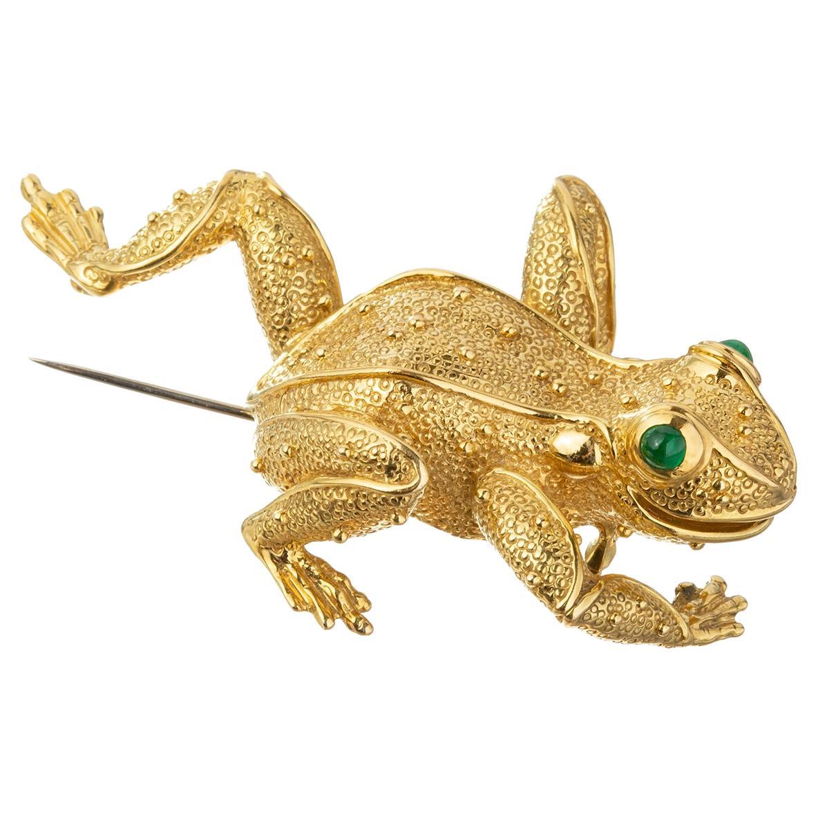 Whimsical leaping frog in textured and polished 18k yellow gold.  Eyes are accented by vibrant green, round faceted, natural emerald eyes.  White gold double pin stem hinged backing.  Measuring 3
