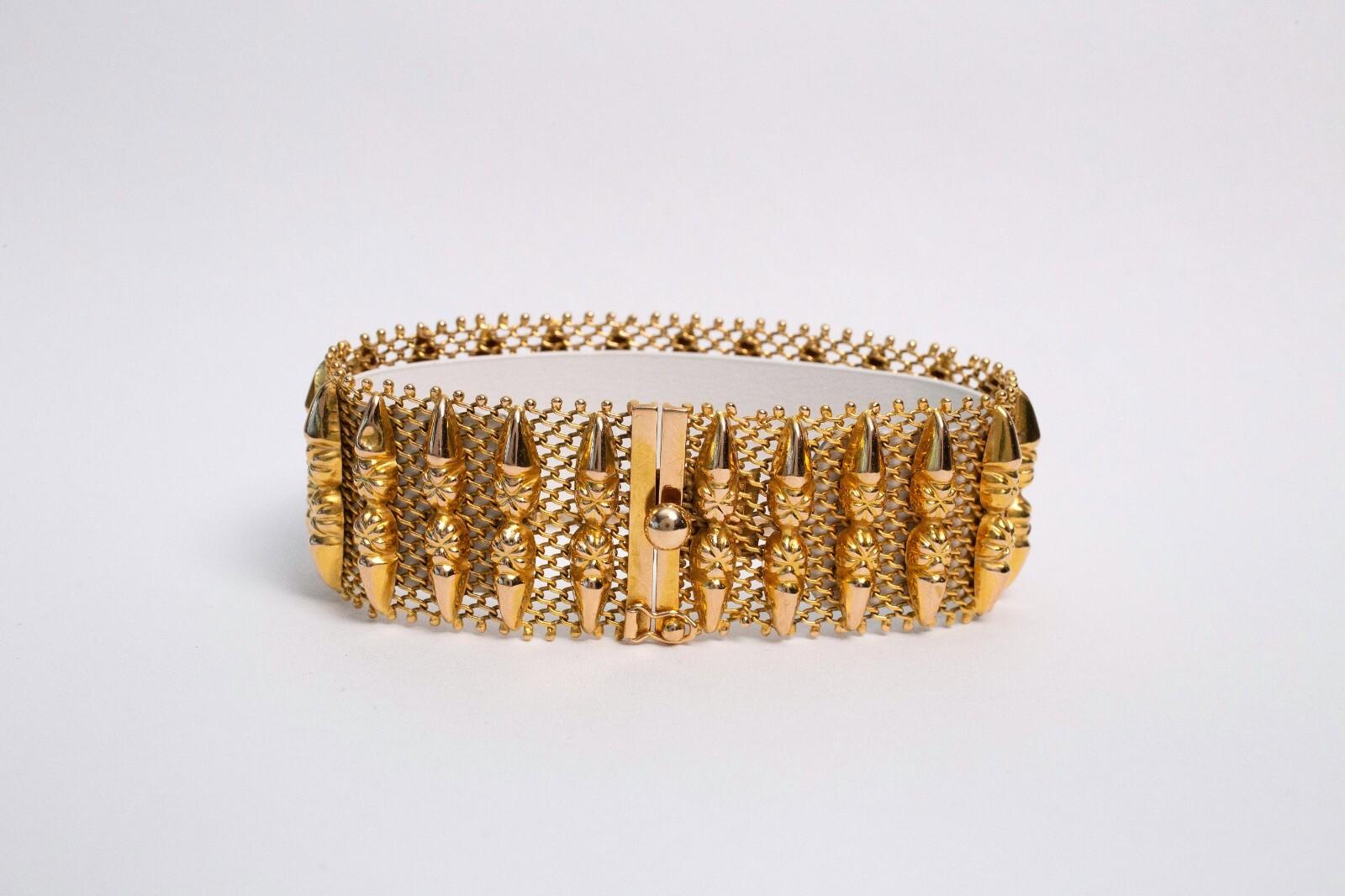 Este llamativo brazalete de oro amarillo de 18 quilates es una atrevida declaración de intenciones que exhibe una intrincada artesanía y un diseño vanguardista. La pulsera presenta una banda en forma de malla, que proporciona flexibilidad y
