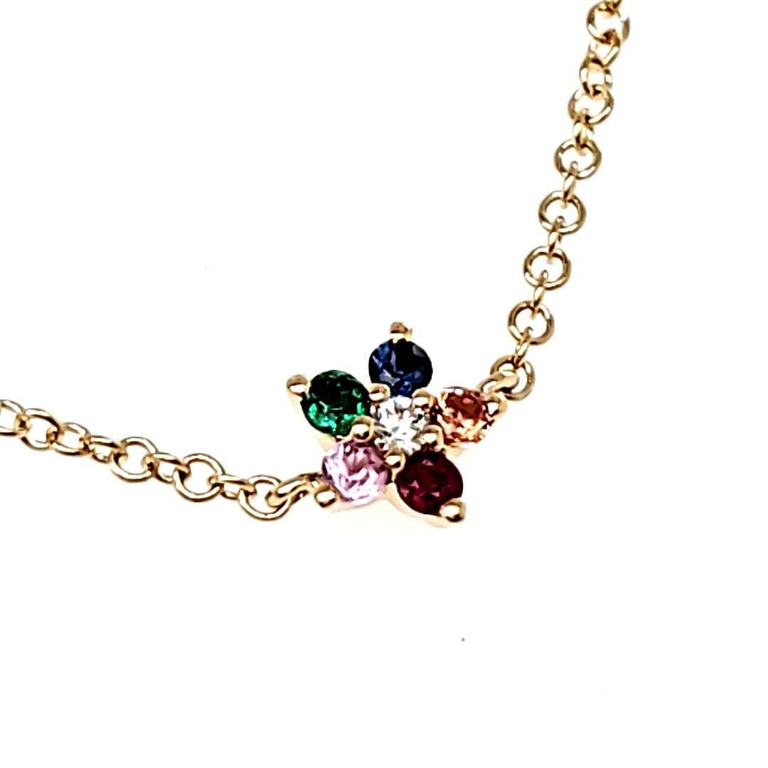 A delicate 0.02 cts of round diamond sparkling at the center is surrounded by five vibrant multi-color stones (0.13 cts) resembling petals – Emerald, Blue Sapphire, Pink Sapphire, Orange Sapphire, and Ruby. 

Suspended from an elegant 18K yellow