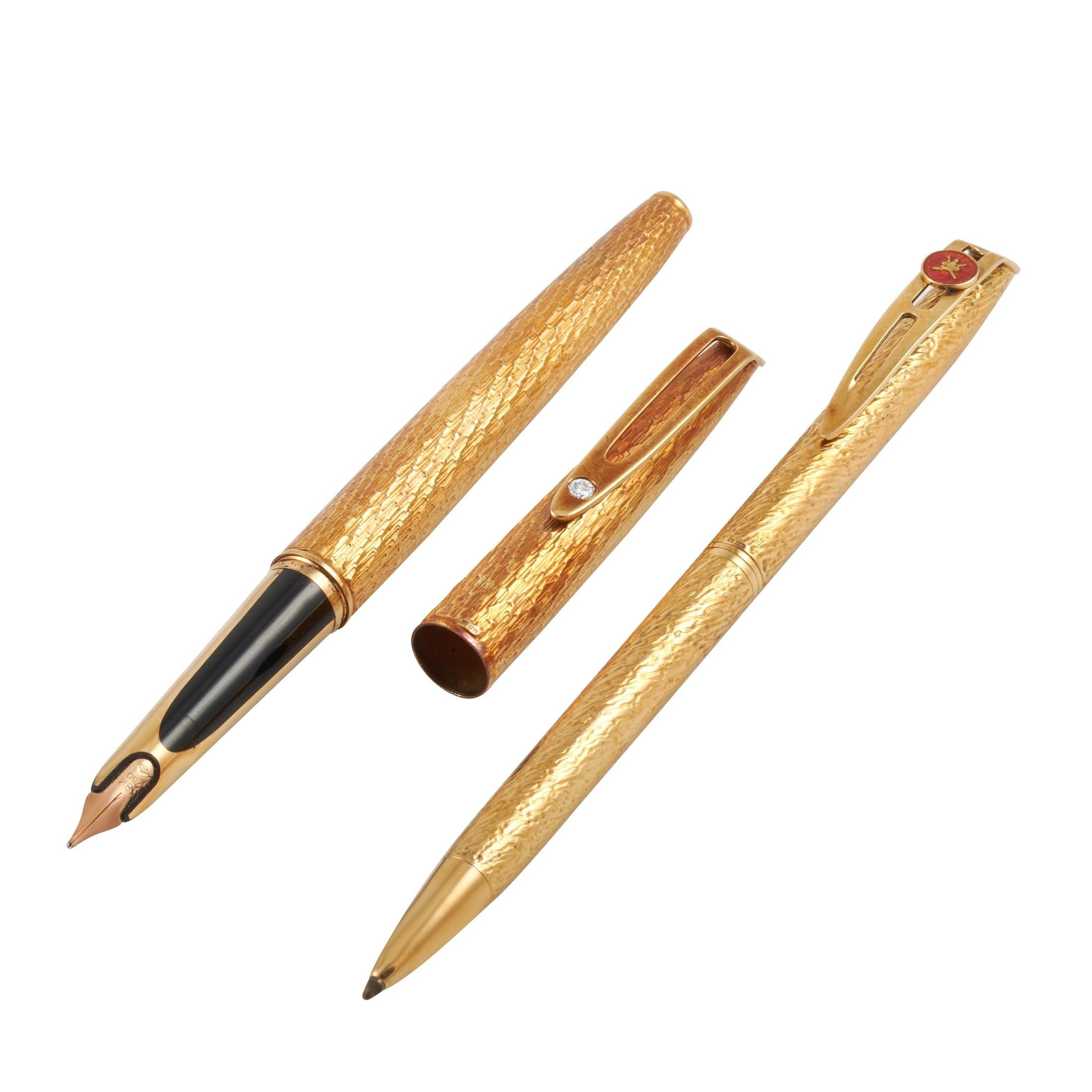 This set of two 18K textured yellow gold pens were made for the Sultan of Oman to give as gifts. One pen features a fountain tip, and the clip is set with a single round diamond. The other pen features a retractable ball point tip, and its cap bears