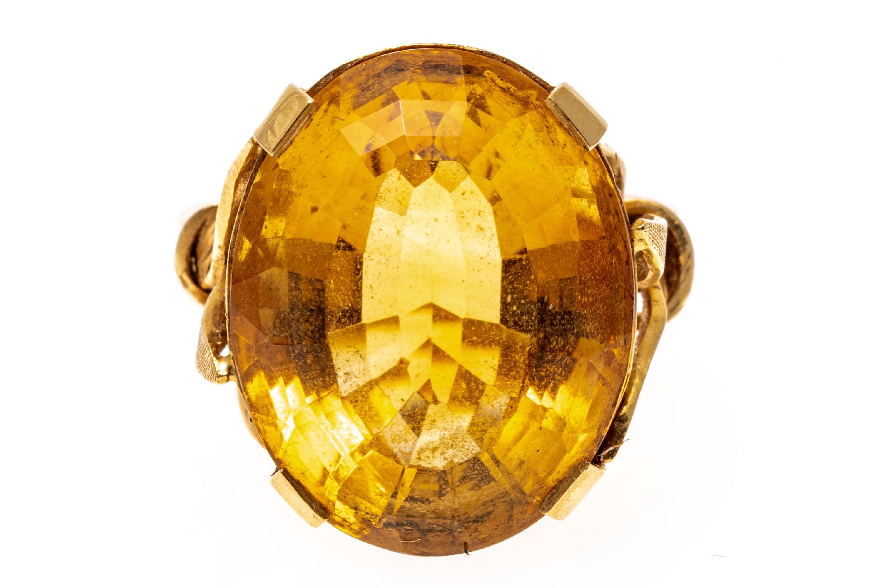 18k yellow gold ring. This delightful ring features a center oval faceted, medium golden yellow color citrine, approximately 13.60 CTS, accented by florentined and high polished gathered foliate shoulders.
Marks: 750
Dimensions: 9/16