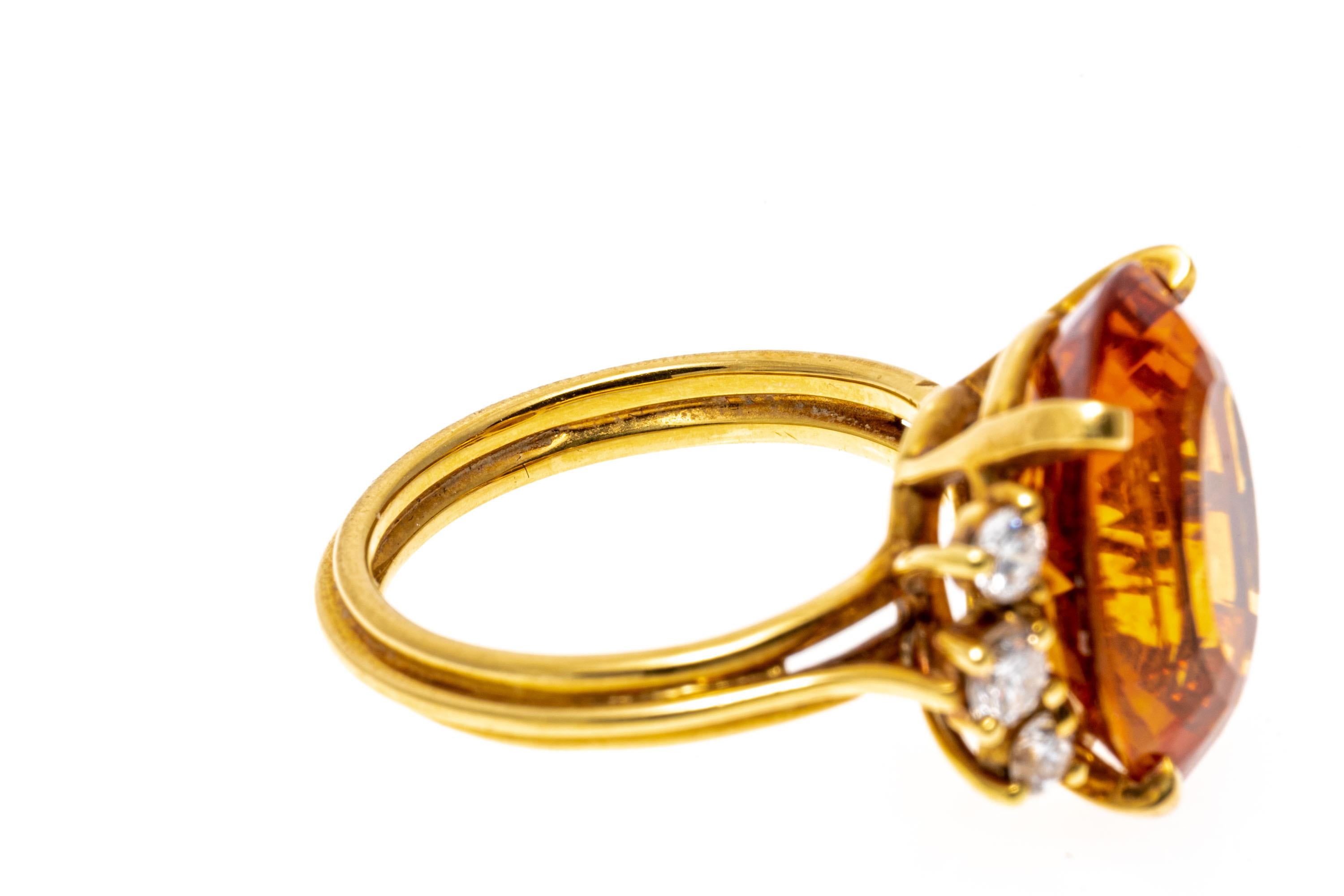 18k yellow gold ring. This delightful ring features a center oval faceted, medium to dark orange color citrine, approximately 7.96 CTS, flanked by graduated round brilliant cut diamonds, approximately 0.32 TCW, prong set. The ring is adorned by a