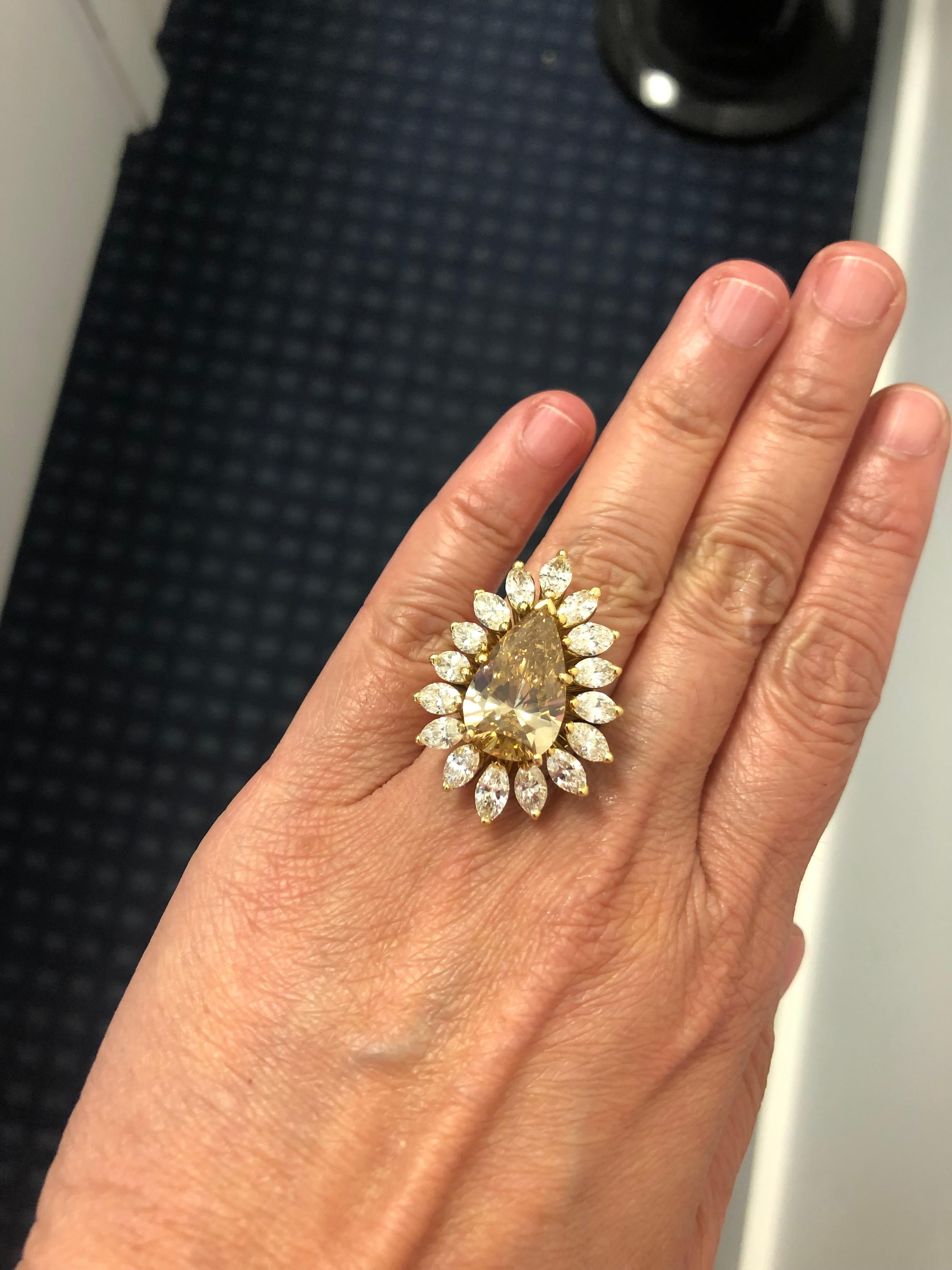 A magnificent ring centering one large pear shaped fancy brown yellow diamond SI1 of natural color, surrounded with a frame of marquise shaped diamonds weighing approximately 7.99 carats, finely mounted in 18k yellow gold. A brilliant ring that