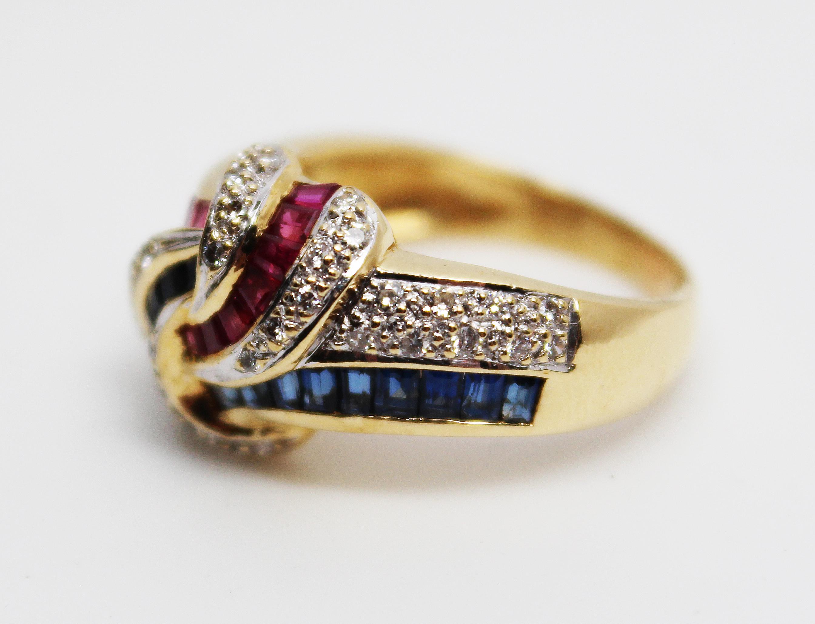 This is a stunning statement ring in 18k yellow gold featuring a bold knot design set with deep red rubies, rich blue sapphires, and sparkling white diamonds. The excellent combination of colored stones paired with the unique knot design makes this
