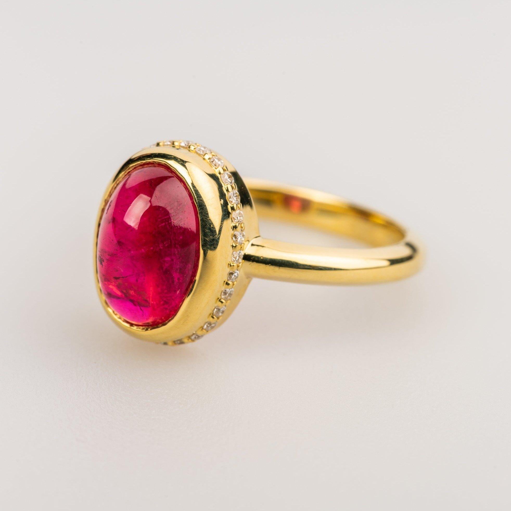 An 18k yellow gold ring featuring one bezel set cabochon red tourmaline, 4.5 carats, and accented by 29- 1mm round full cut white diamonds for a total of .145 carats, F color VS clarity. Ring size 6.75. This ring was made and designed by Sydney