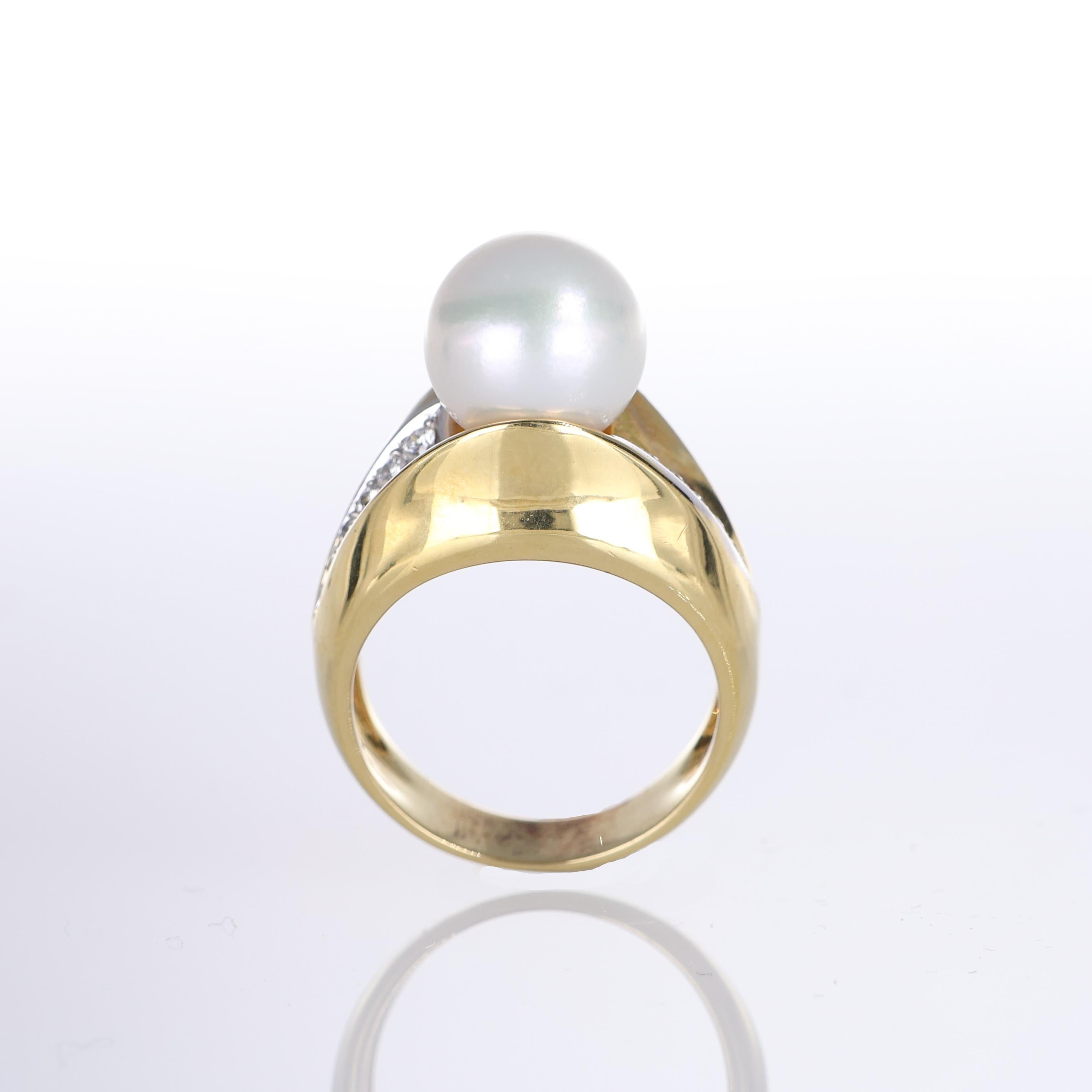 A bold and elegant 18k yellow gold ring featuring a luminous central pearl, framed by two delicate rows of brilliant-cut diamonds totaling 0.21 carats. The fluid gold setting enhances the natural beauty of the pearl, creating a refined yet striking