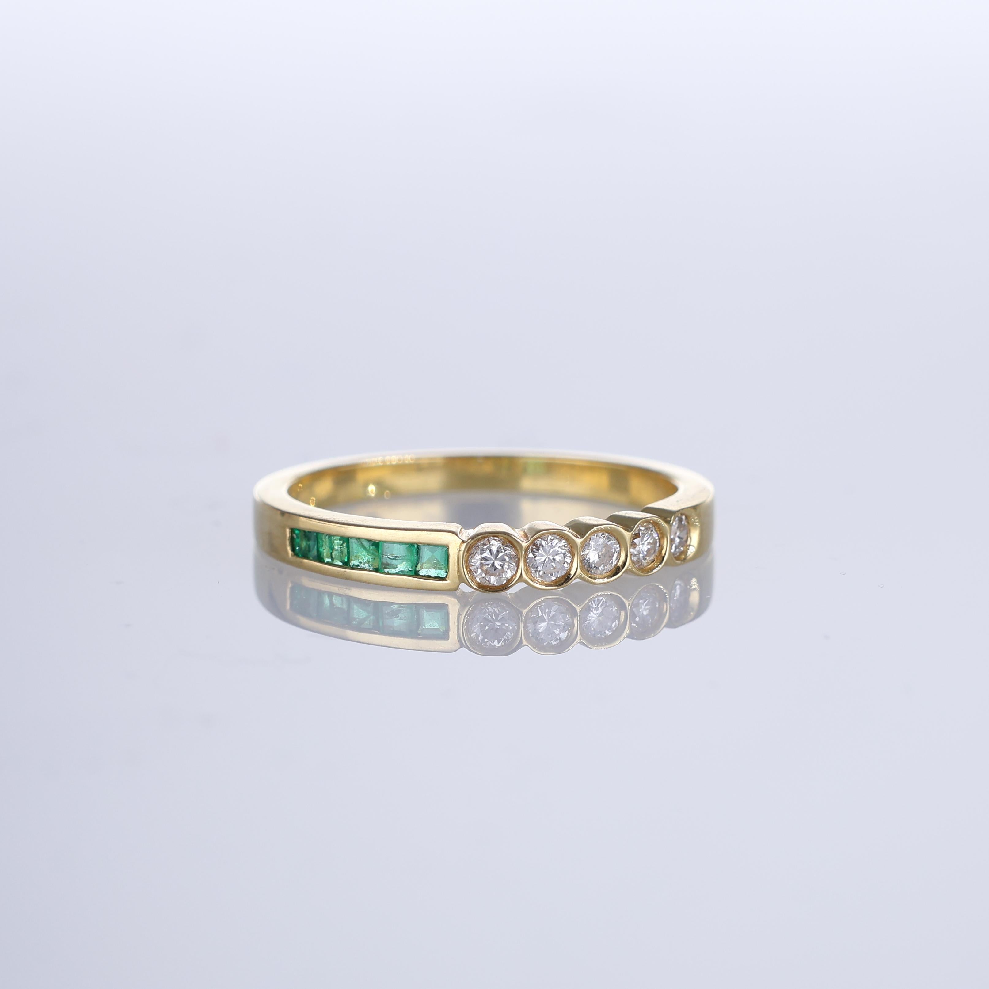 A refined 18k yellow gold Riviera ring featuring a unique asymmetrical design. One side showcases a row of baguette-cut emeralds, while the other is adorned with brilliant-cut diamonds, creating a striking contrast. The vibrant green of the emeralds