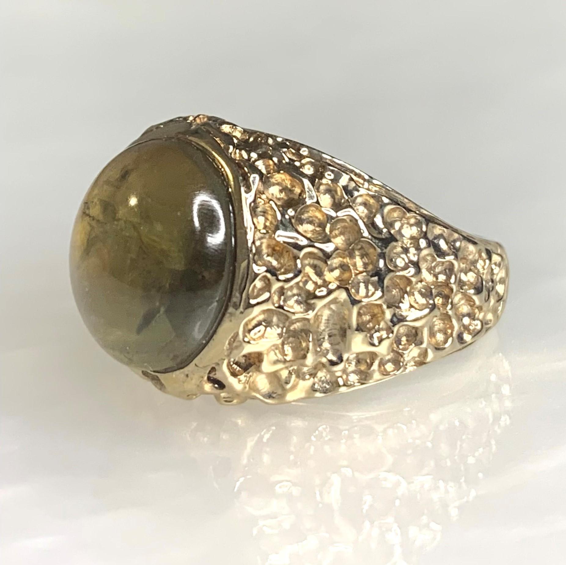 A noticeable and unusual vintage Cat's Eye ring featuring a cabochon cut 14.86 carat center stone secured by a bezel setting surrounded by intricately detailed solid 18k yellow gold.

*Approximate Stone Dimensions: 13mm all around

*Approximate ring