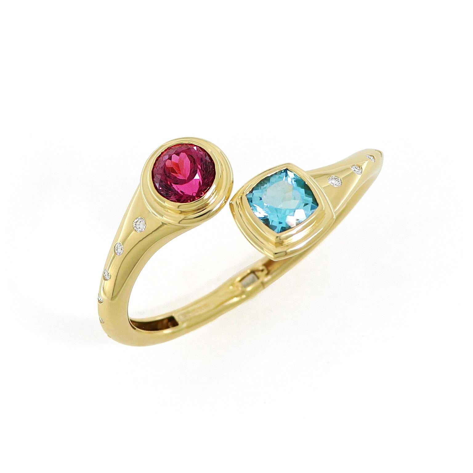 Rubellite and blue topaz are a complementing duo for this 18k yellow-gold bangle bracelet. One end features a round rubellite, enhancing a brilliance of red and warm pink. The other end features a square cushion blue topaz, contrasting its