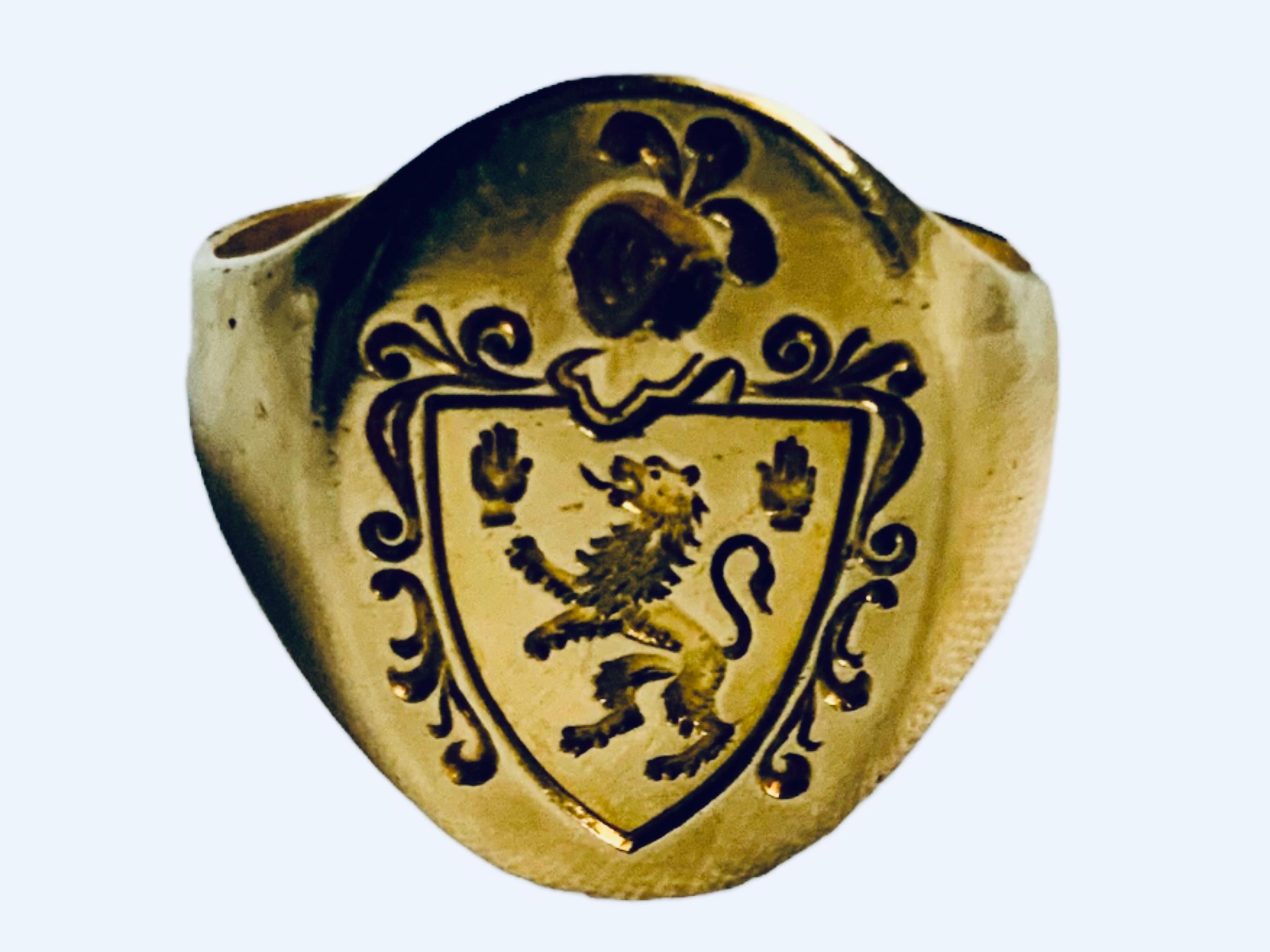 This is an 18K Yellow Gold Signet Heraldic Ring. It depicts a gold ring that has an oval shaped top embellished with an engraved family’s crest or coat of arms. Inside the shield, there is a lion rampant and two hands engraved. A armor helmet