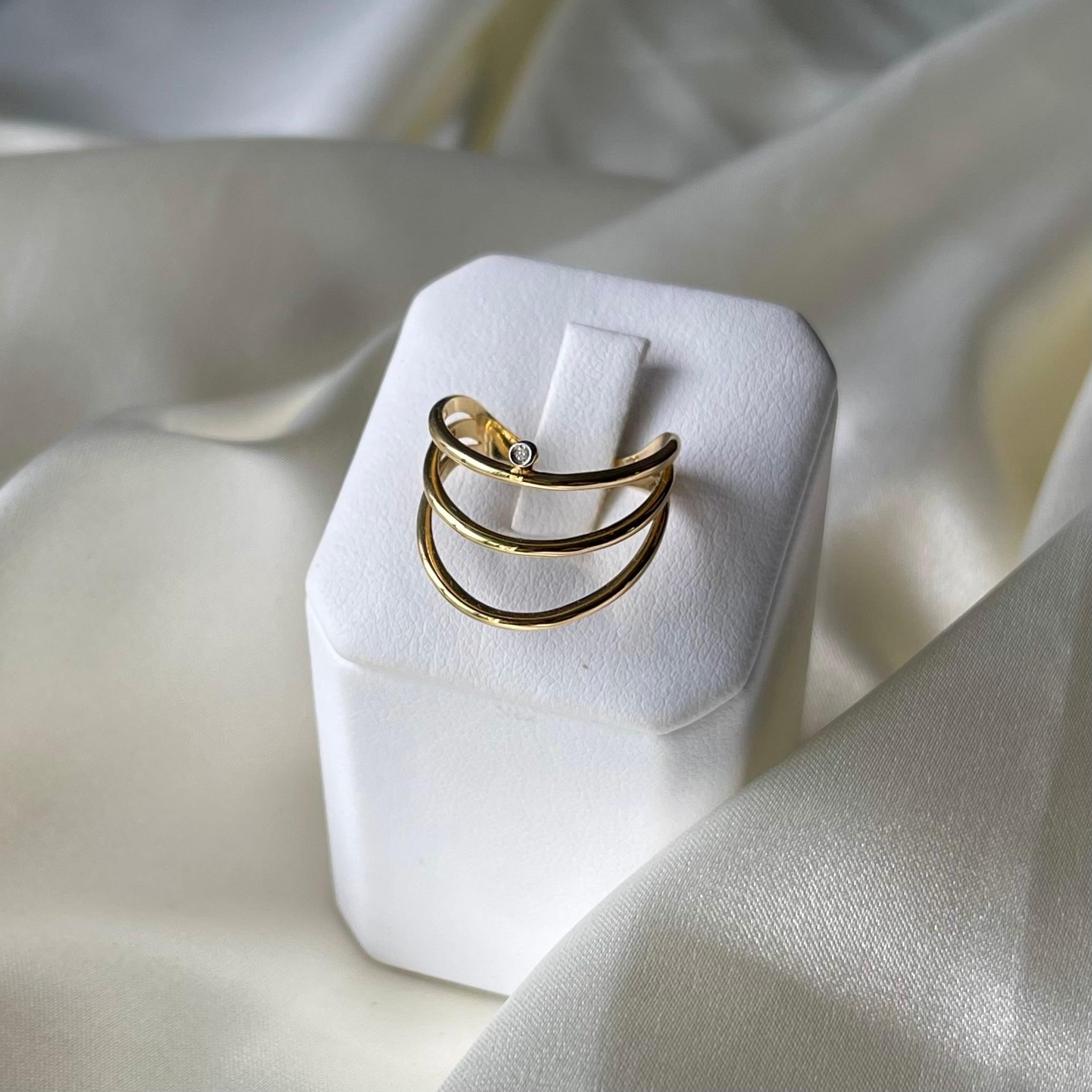This bold and modern 18K yellow gold spiral ring features a unique multi-band design that wraps elegantly around the finger. A single diamond accent is set into one of the spirals, adding a touch of sparkle to the sleek and contemporary silhouette.