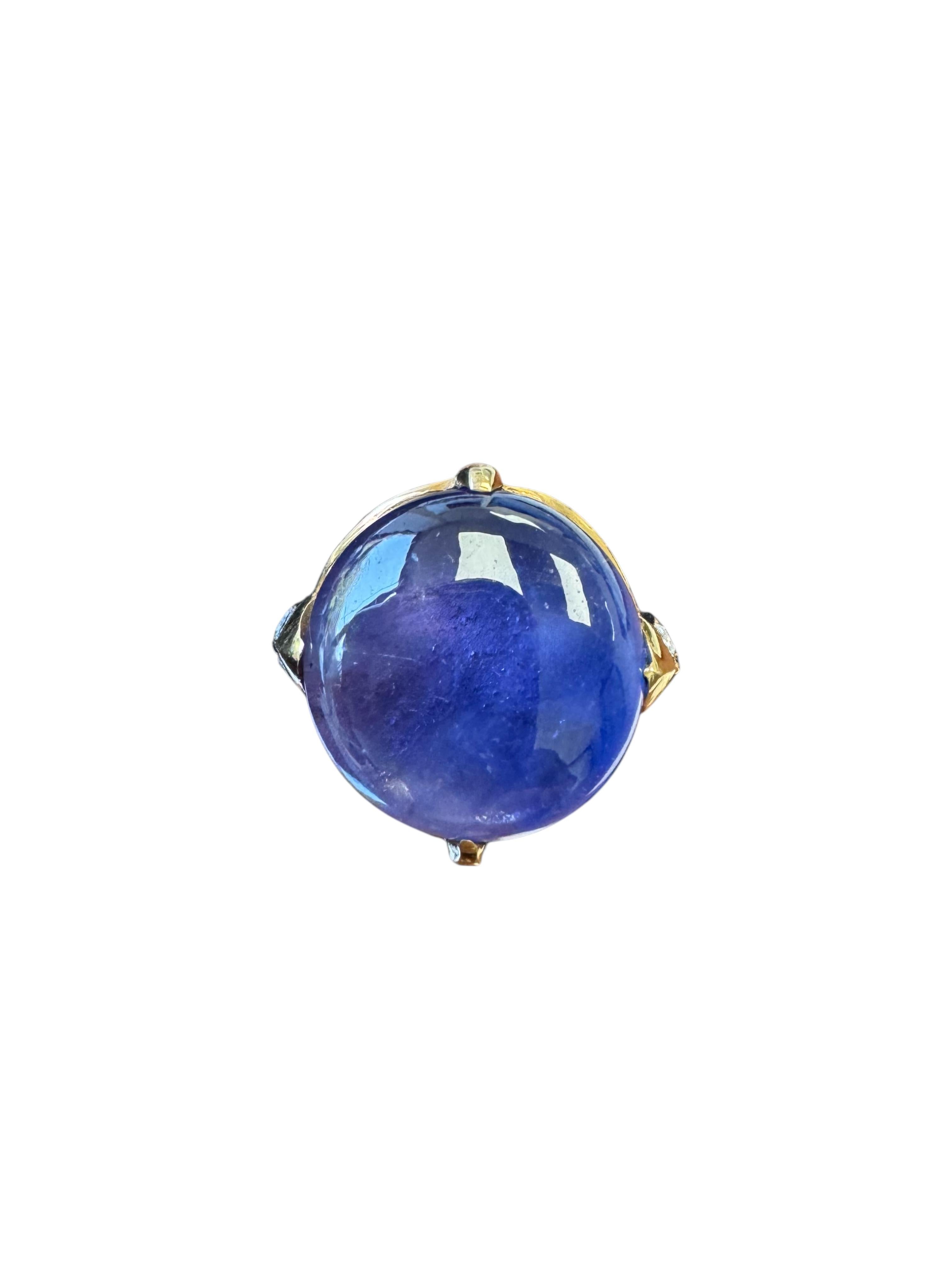 A luminous vintage ring showcasing a mesmerizing 12.49 carat deep violet-blue star sapphire cabochon, set in rich 18K yellow gold. The sapphire exhibits a distinct asterism, gracefully accented by .51 carats of tapered baguette-cut diamonds along