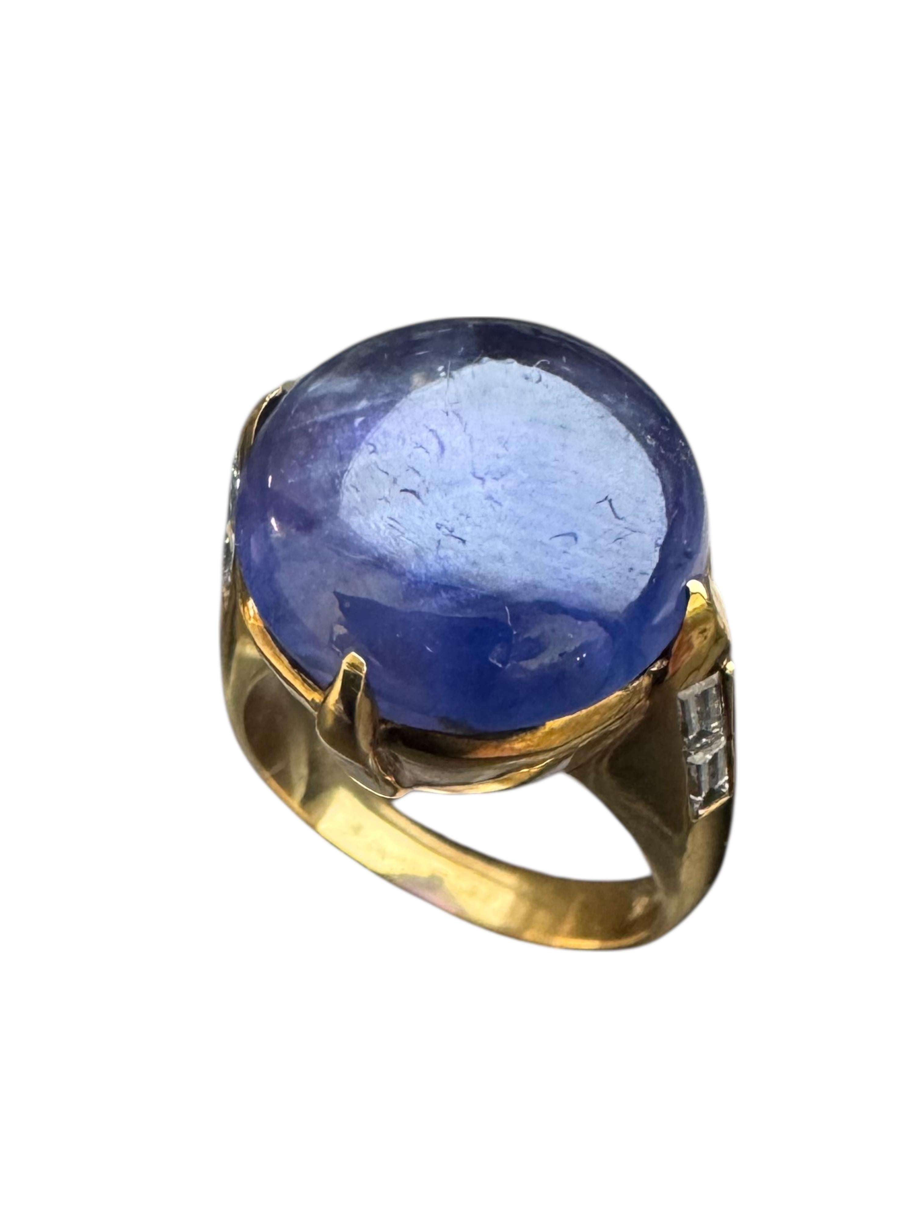 Cette bague vintage lumineuse met en valeur un saphir étoilé bleu-violet de 12,49 carats, serti dans de l'or jaune 18 carats. Le saphir présente un astérisme distinct, gracieusement accentué par 0,51 carat de diamants taille baguette effilés le long