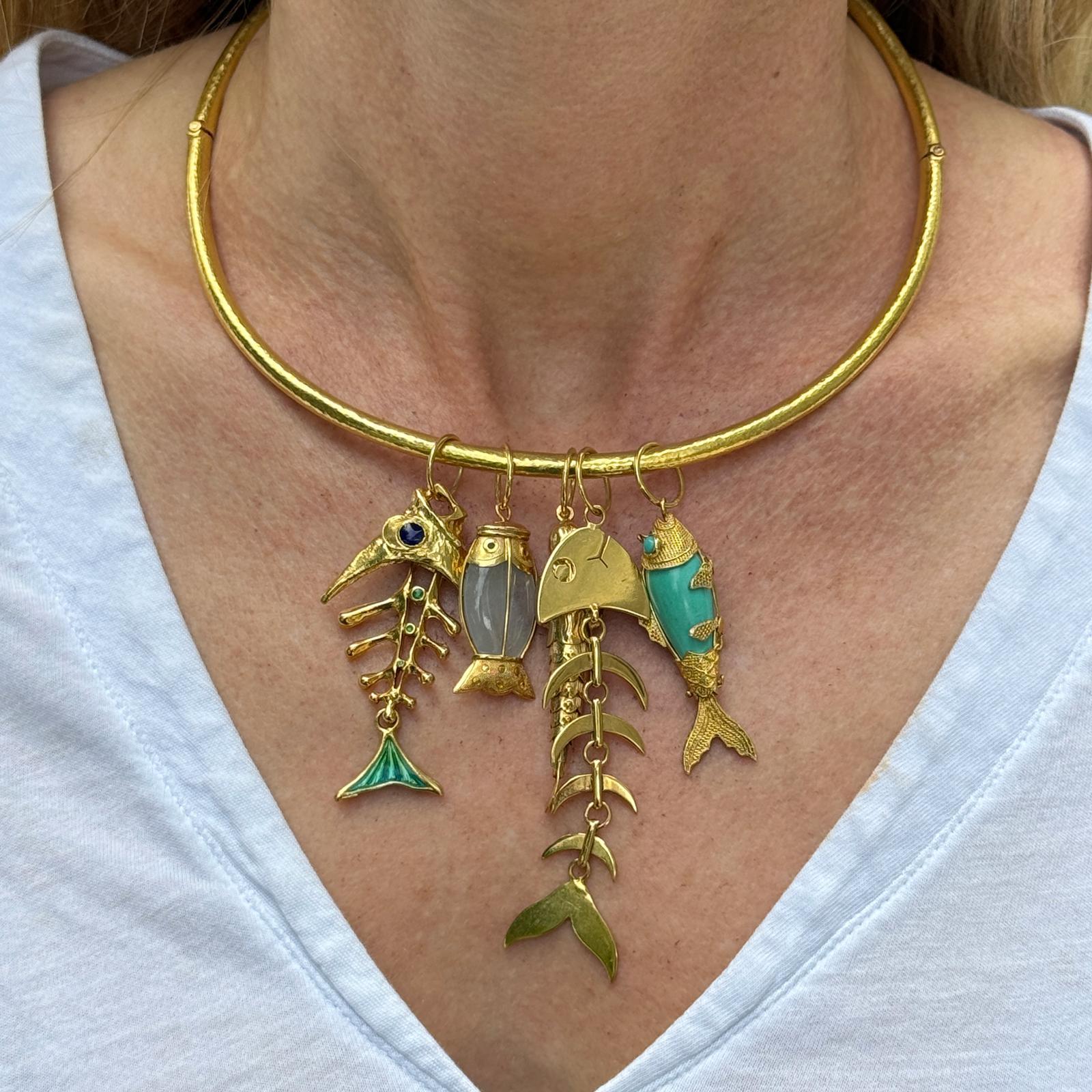 The 18K Yellow Gold Textured Necklace by Elana Hadjidakis is a captivating piece featuring an intricate design and exquisite details. Adorned with five charming fish pendants, each embellished with vibrant enamel or turquoise gemstones, this