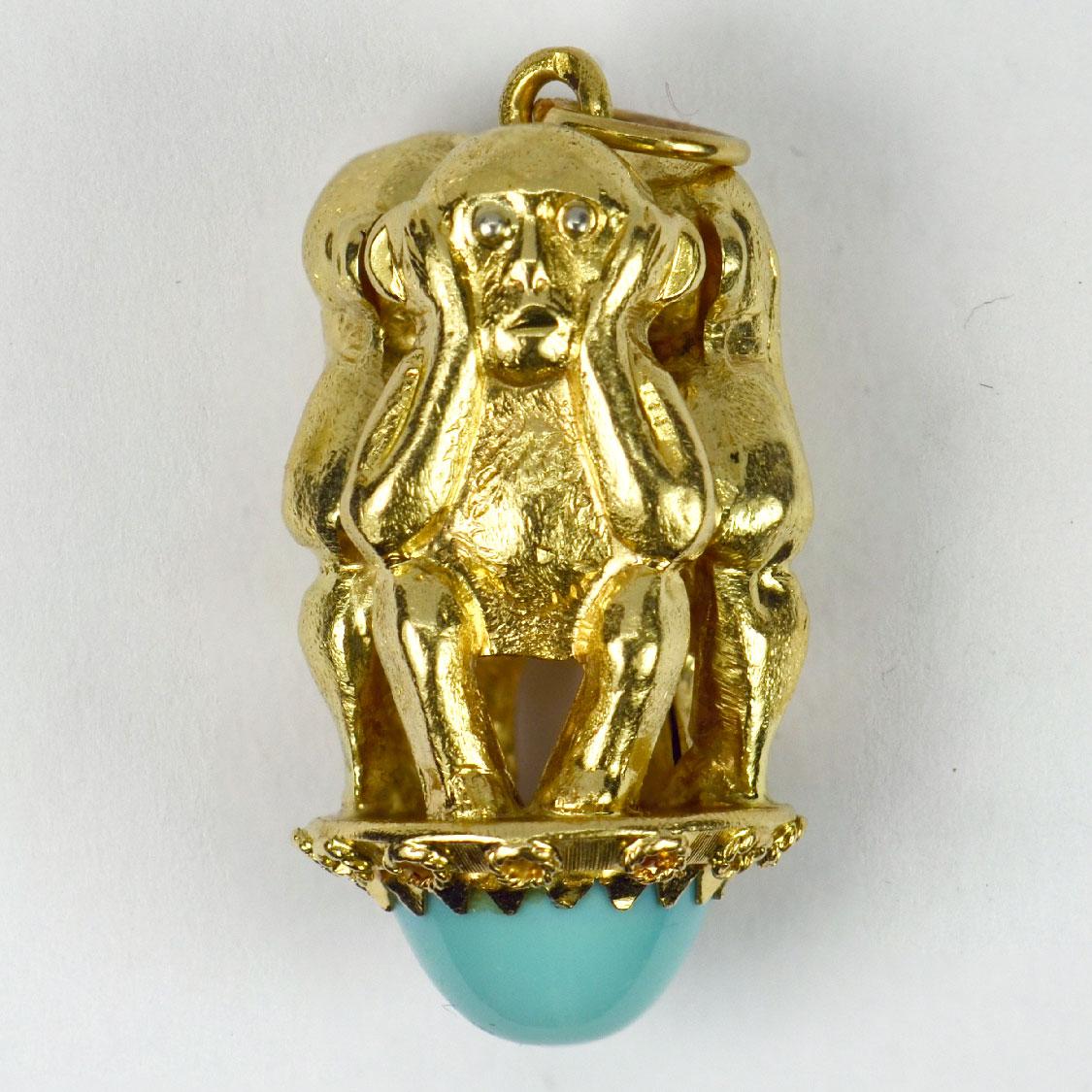 An 18 karat (18K) yellow gold charm pendant designed as the three wise monkeys covering their eyes, ears and mouth, symbolising the mantra ‘See no evil, hear no evil, speak no evil’. The monkeys stand atop a large turquoise cabochon estimated to